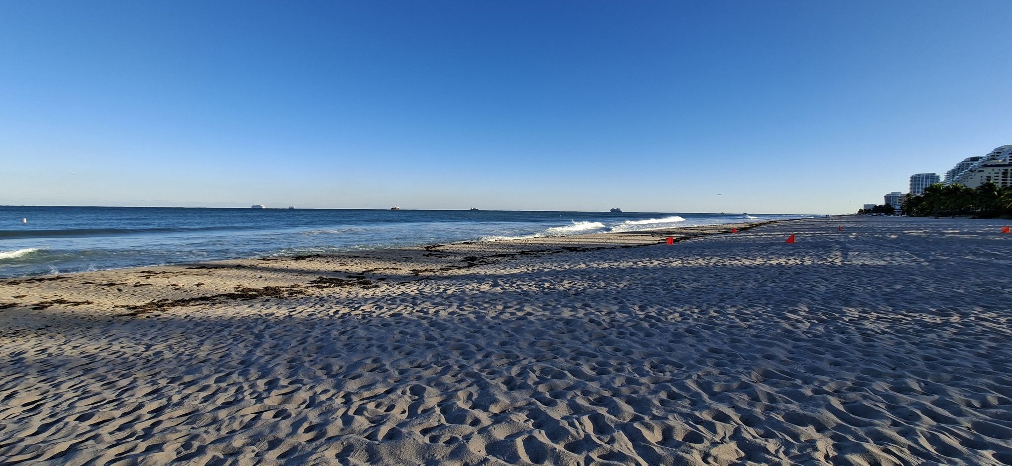 Panoramic view of a wide, empty beach with gentle waves under a clear sky. - Running loop from A1A/Northeast 30th Street