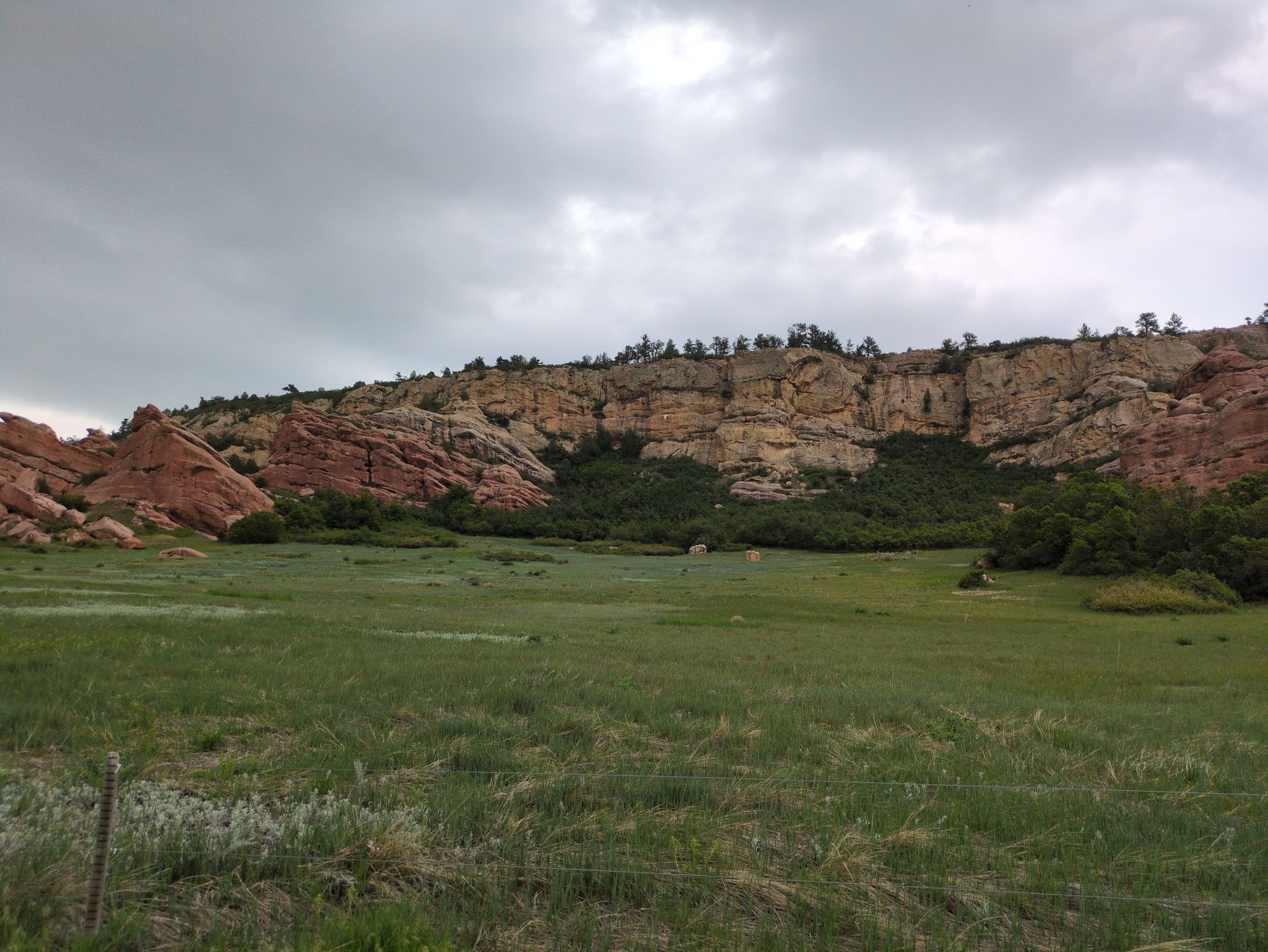 A wide green field in front of towering red and tan rock cliffs. - Coyote Song Trail – Grazing Elk Trail loop from Classification Natural Resource Protection
