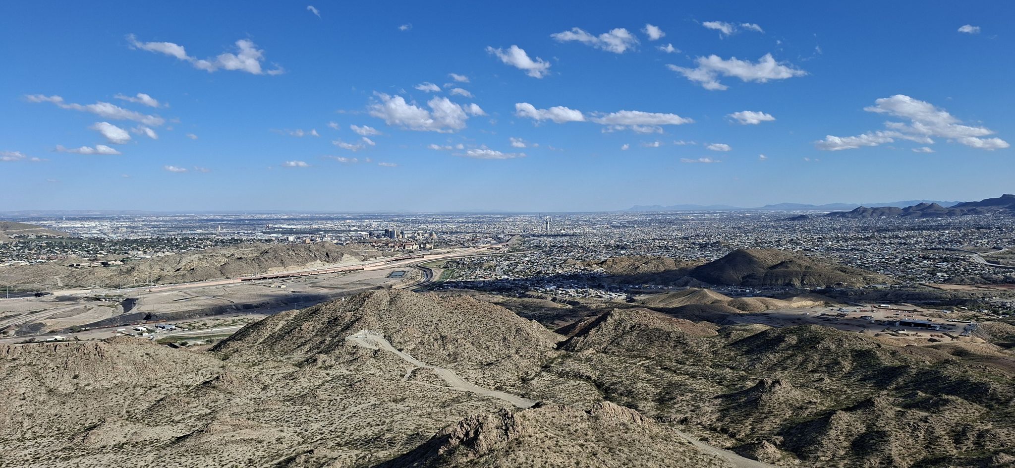 Panoramic view of arid hills overlooking a sprawling city under a blue sky. - Mount Cristo Rey Trail
