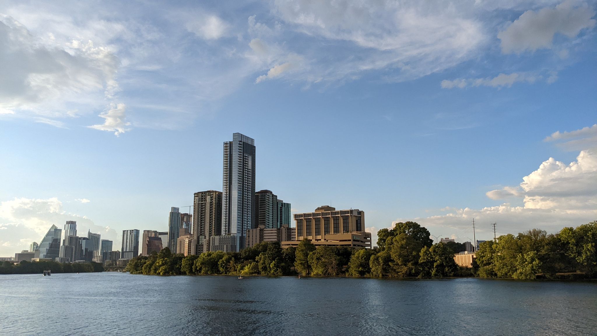 City skyline across a wide river under a partly cloudy sky. - Ann & Roy Butler Hike and Bike Trail