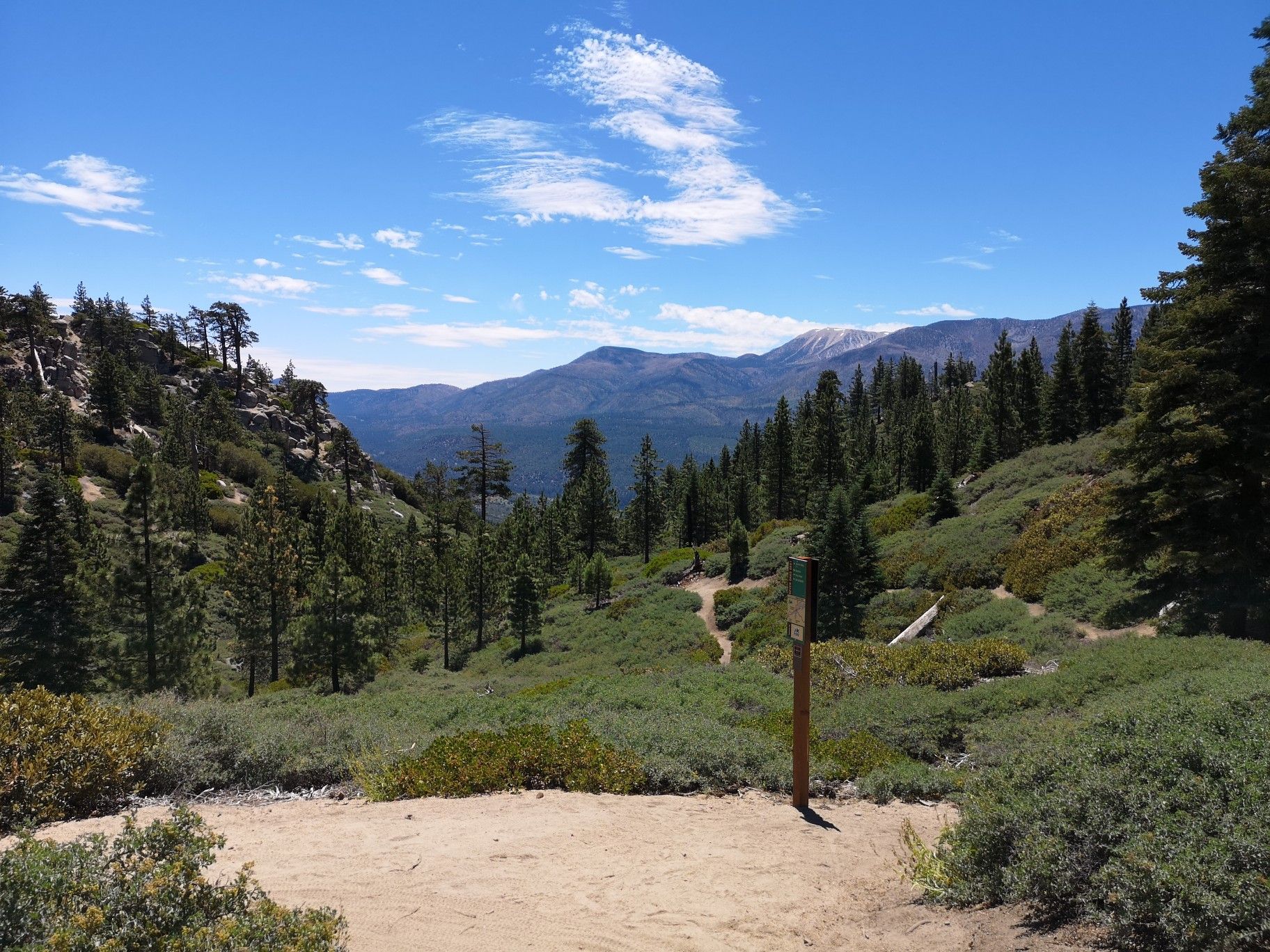 Dirt clearing leading to a forest path with distant mountains under blue sky. - Pine Knot Trail to Grand View Point