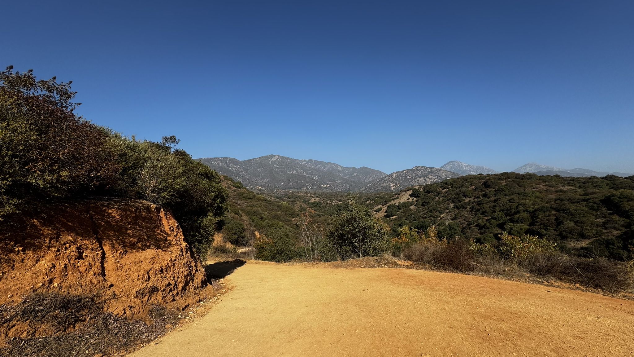 Wide dirt path overlooking green mountains under a clear blue sky. - Claremont Hills Wilderness Park loop