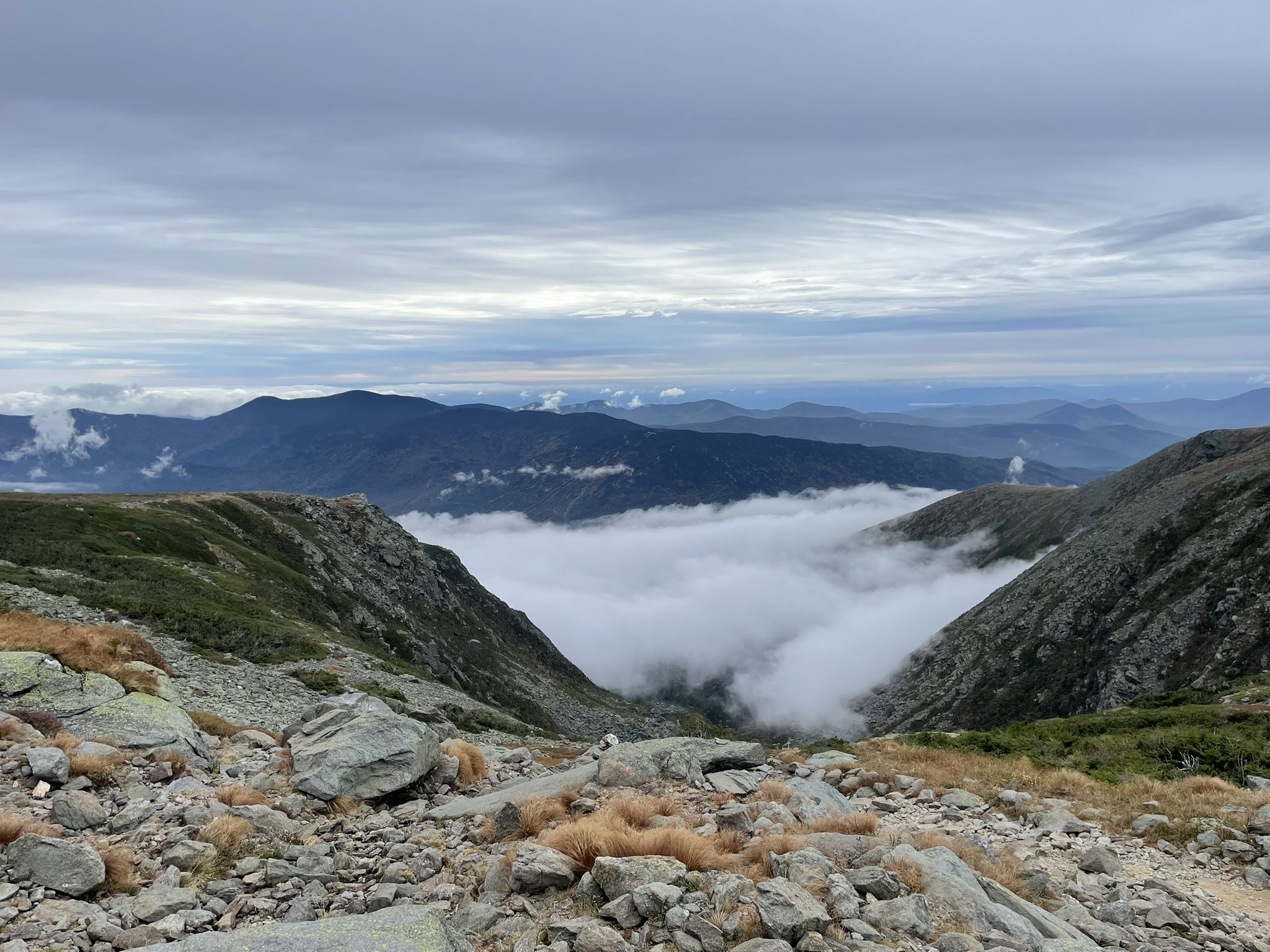 Overcast mountain valley with clouds filling the basin, rocky foreground. - Mount Washington via Tuckerman Ravine Trail