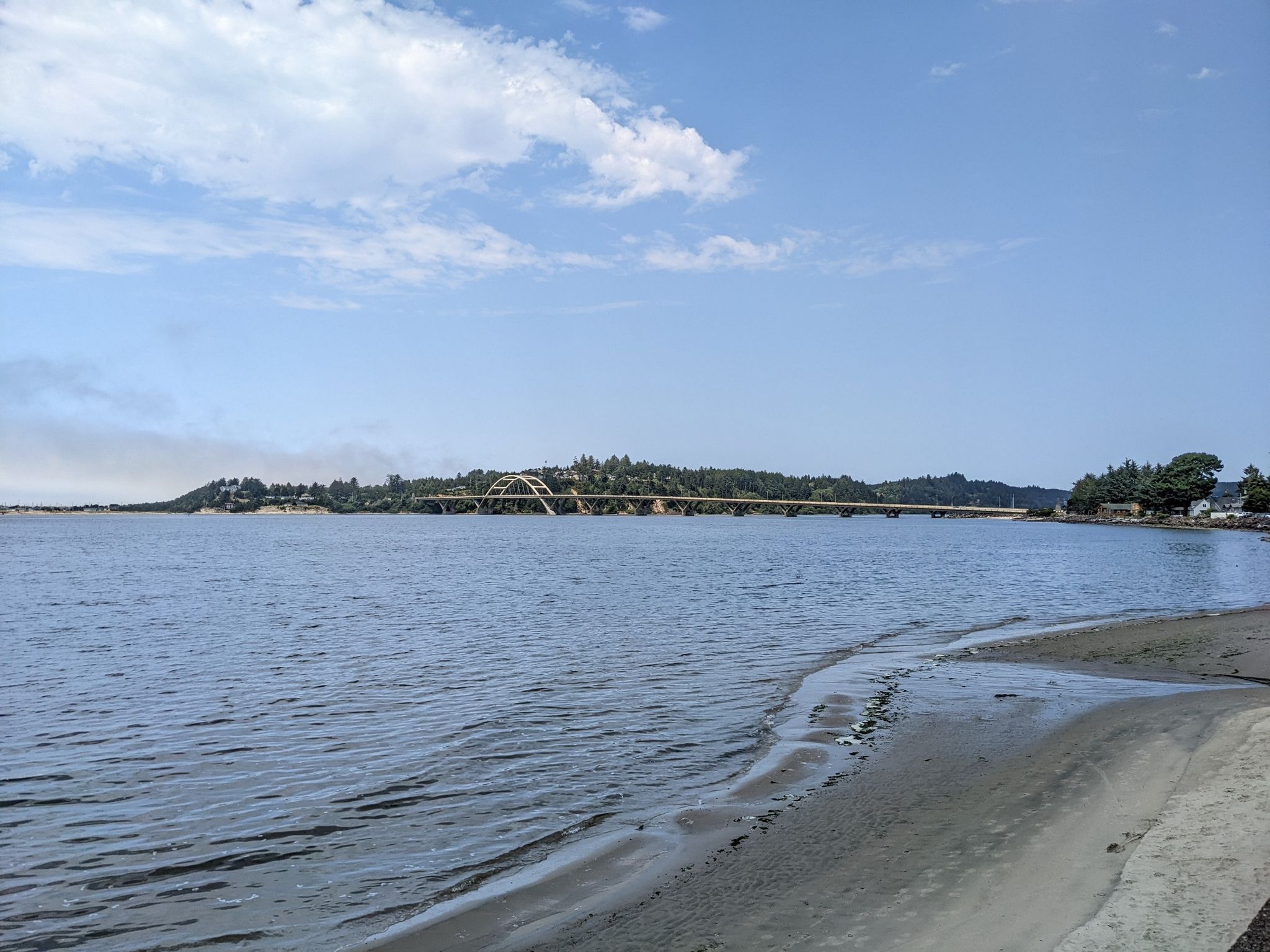 Calm water with a sandy edge, leading to a distant bridge and forested shore. - Big Stump loop from Waldport