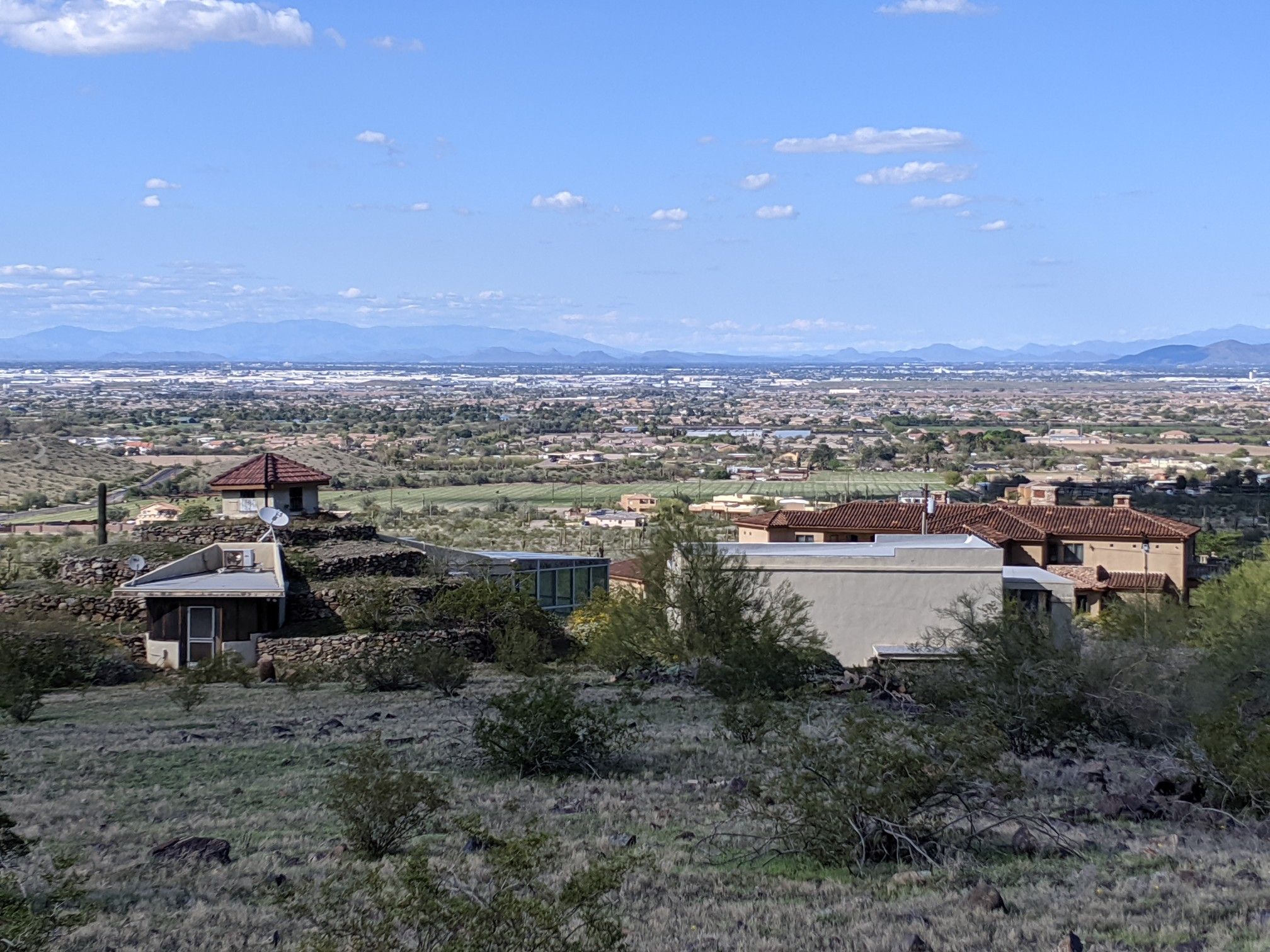 Houses on a desert hillside overlooking a distant city under a partly cloudy sky. - Alta and Ma-Ha-Tuak Perimeter Loop