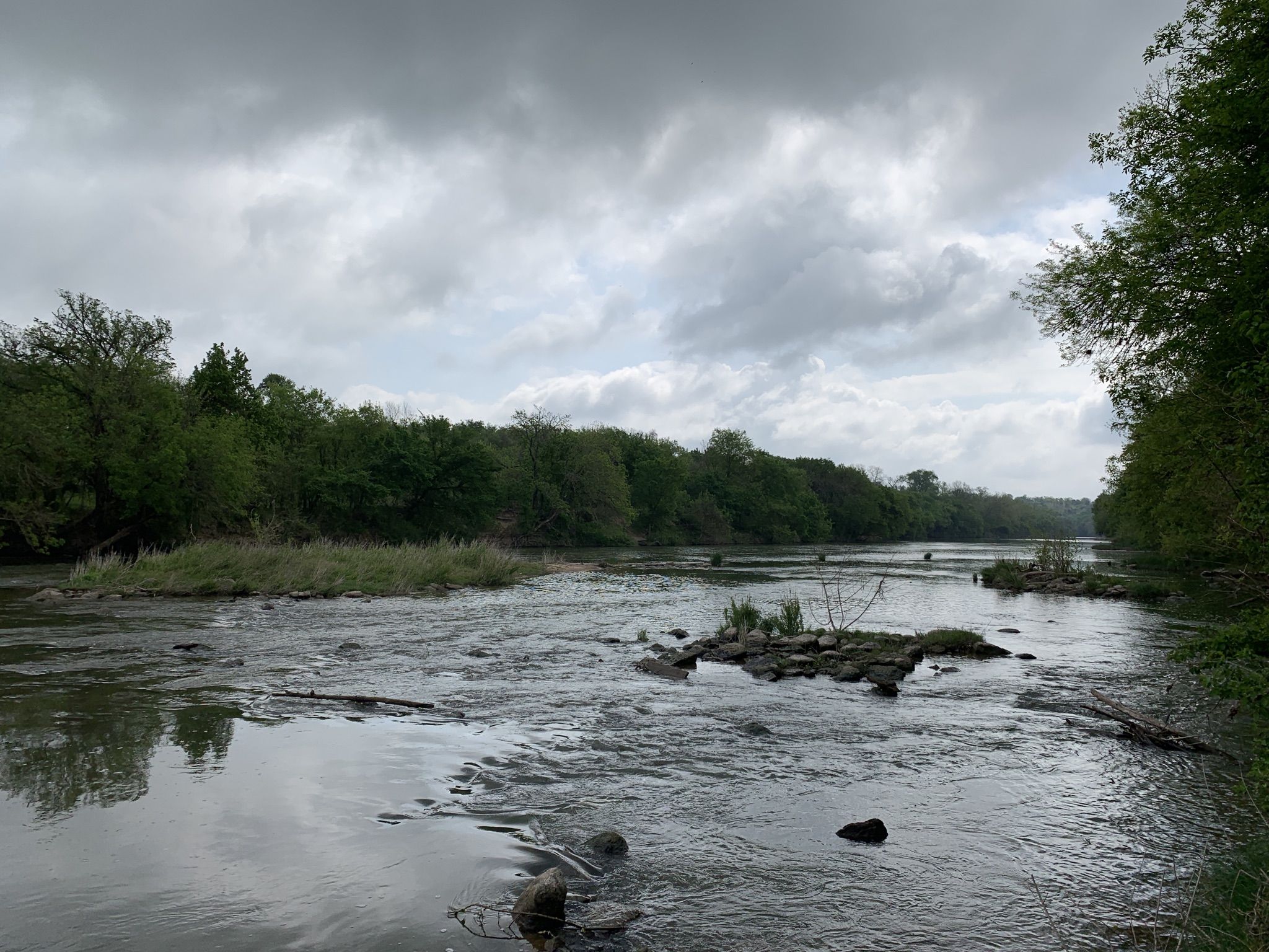 Wide river flowing under an overcast sky, flanked by dense green trees. - McKinney Roughs Loop Trail