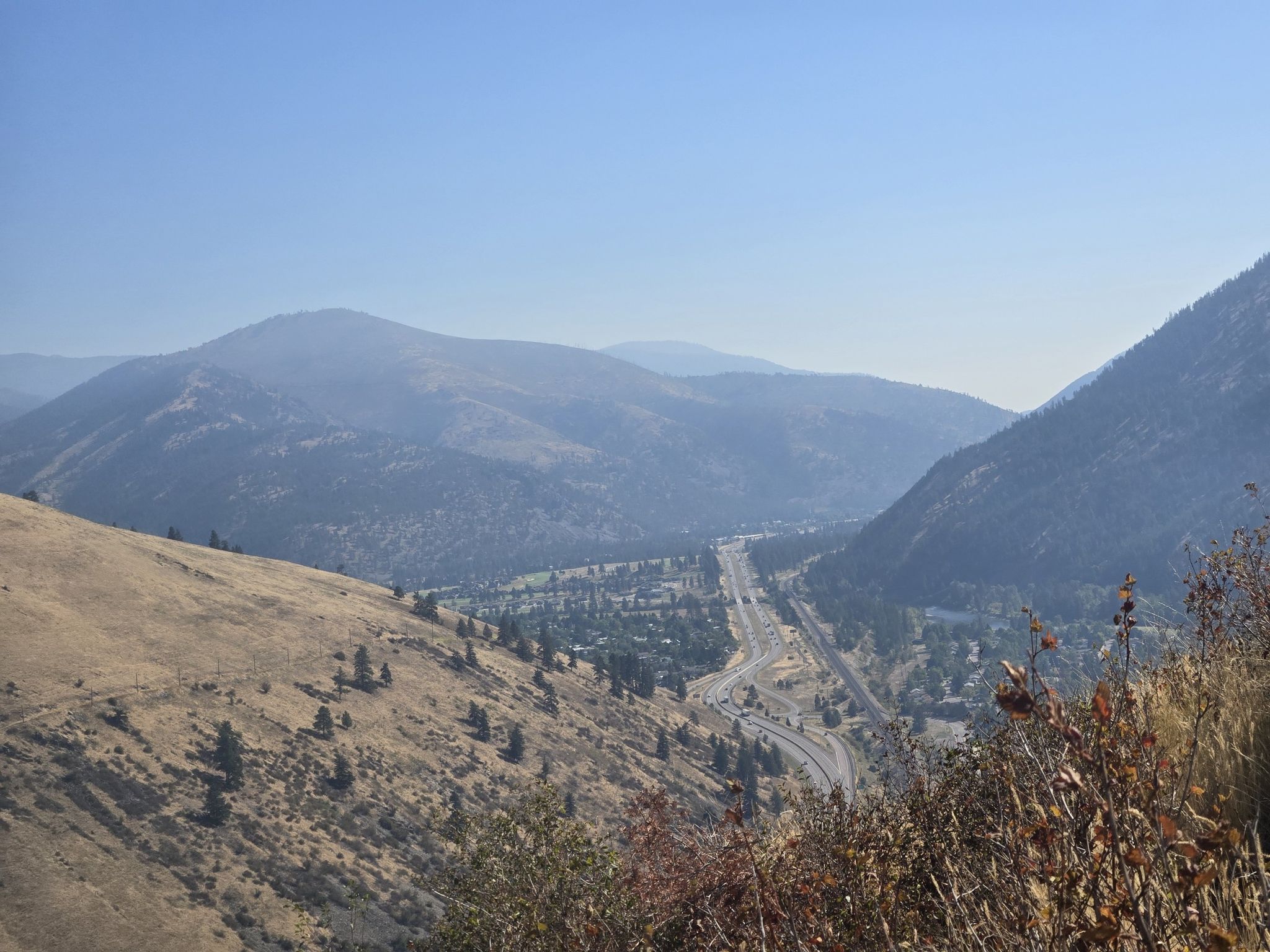 Panoramic view of a valley with a highway, river, and distant mountains. - Jacob's Island – University Mountain loop from Missoula