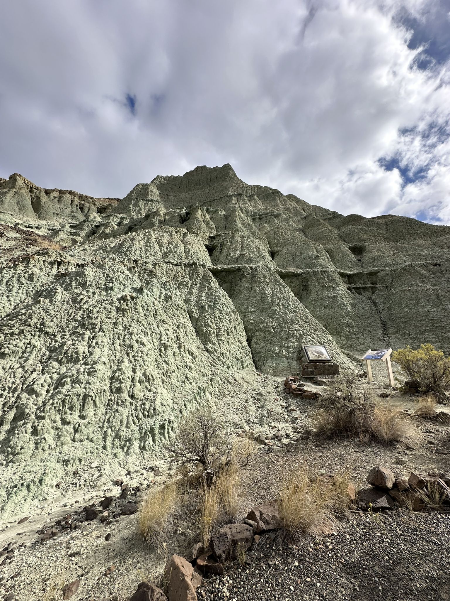 Eroded light green rock formations under a cloudy sky, with arid ground. - Island in Time Trail
