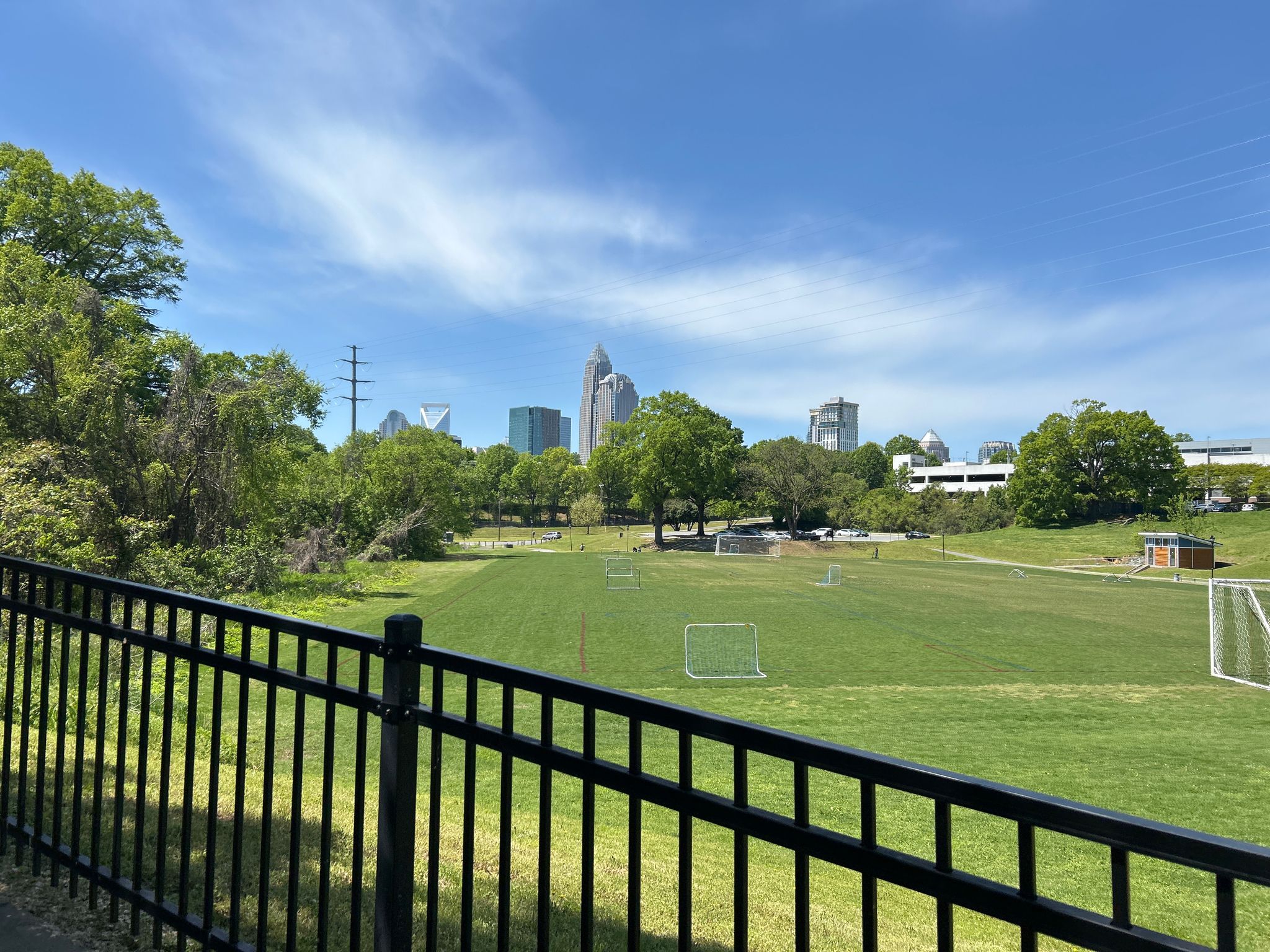 Bright, sunny view of a green park field with a distant city skyline. - Little Sugar Creek Greenway: Cordelia Park