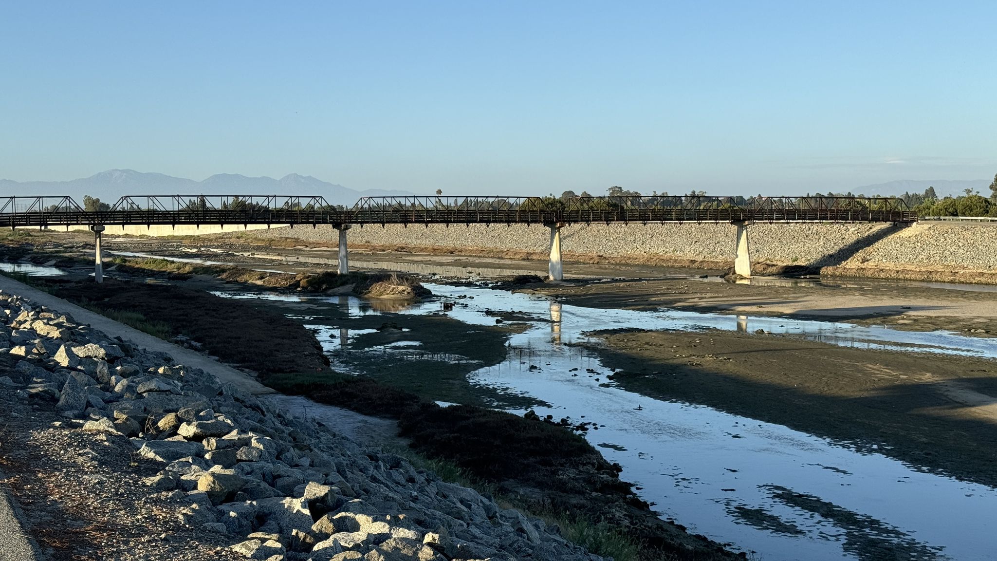 A long metal bridge spans a muddy riverbed under a clear sky. - Least Tern Natural Preserve – Santa Ana River Trail loop from Orange Coast College