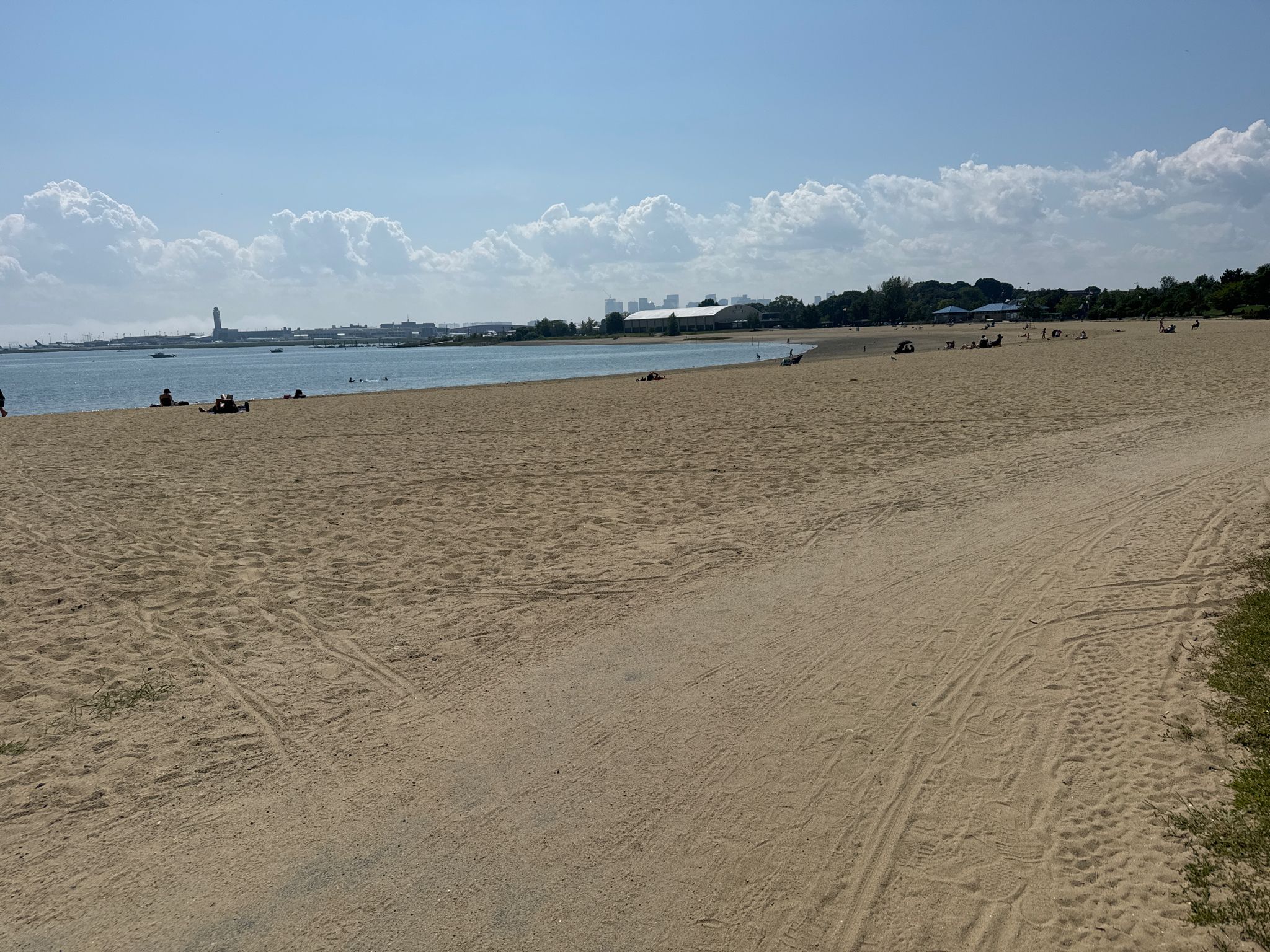 Expansive sandy beach with people, ocean, and a distant city under blue sky. - East Boston Memorial Park loop from Orient Heights