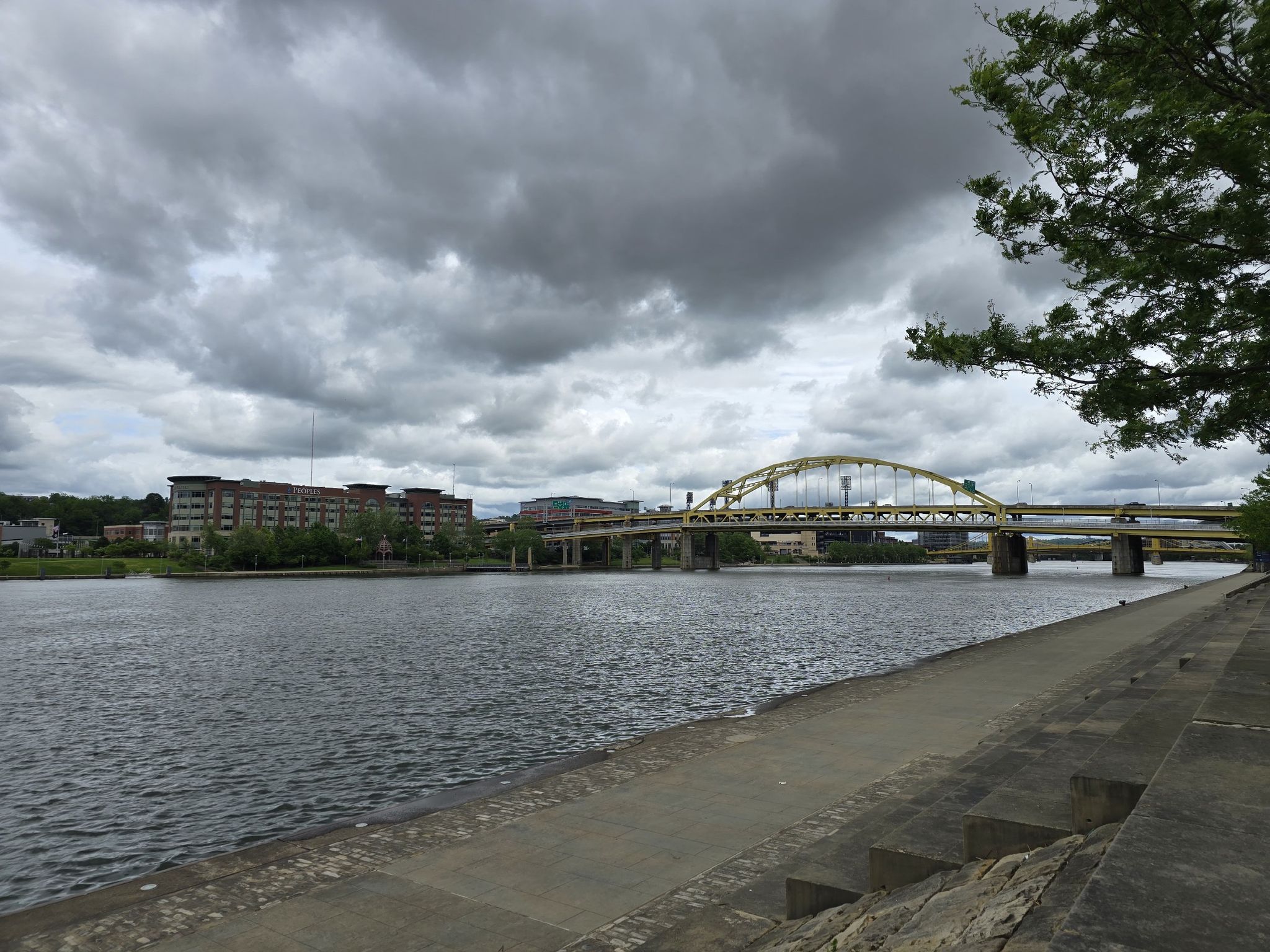 River with a yellow arched bridge and concrete embankment under cloudy skies. - Fort Pitt Block House – Point State Park Fountain loop from Pittsburgh