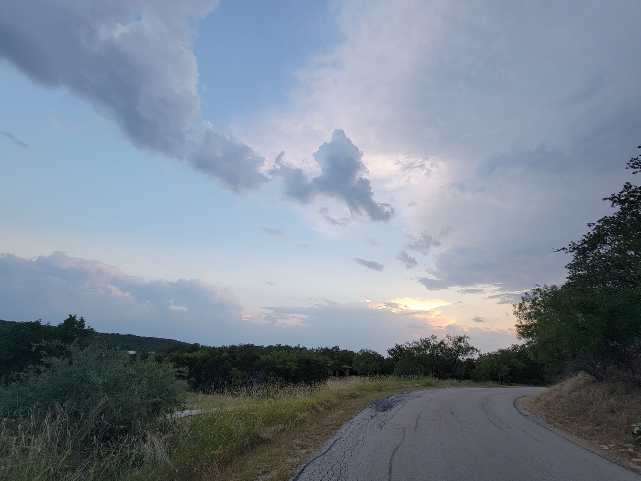 Winding road through a green landscape under a cloudy sunset sky. - Blue Waterfront Trail