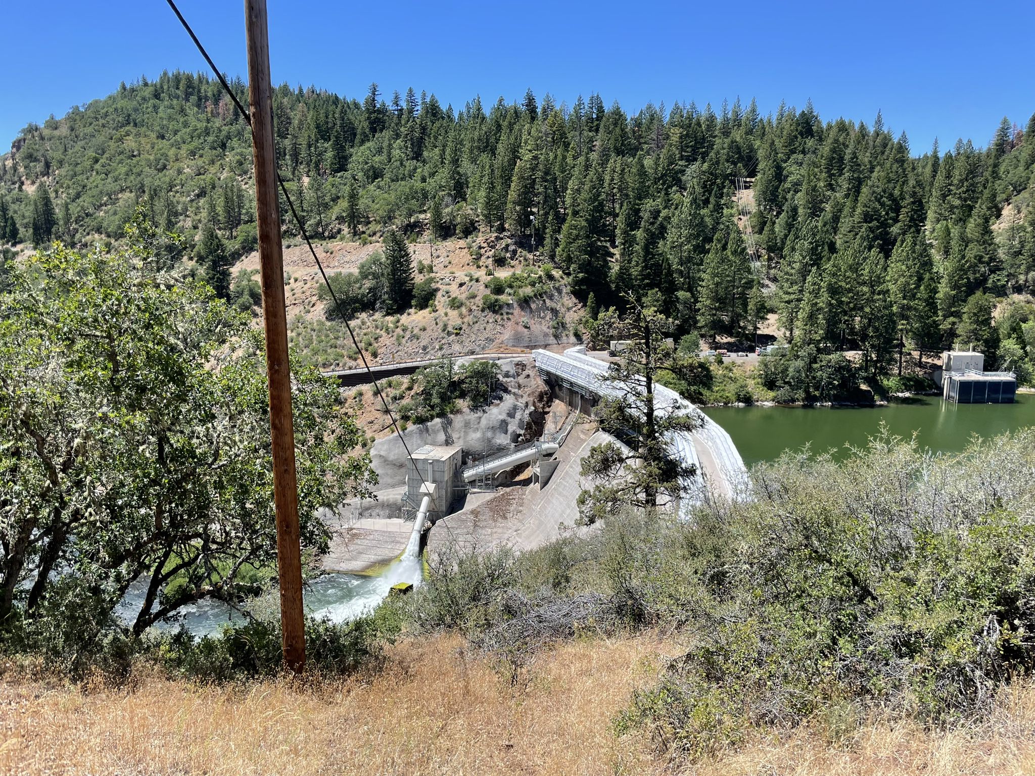 A large concrete dam with water flowing, next to a calm green reservoir. - Pacific Crest Trail: California Section O