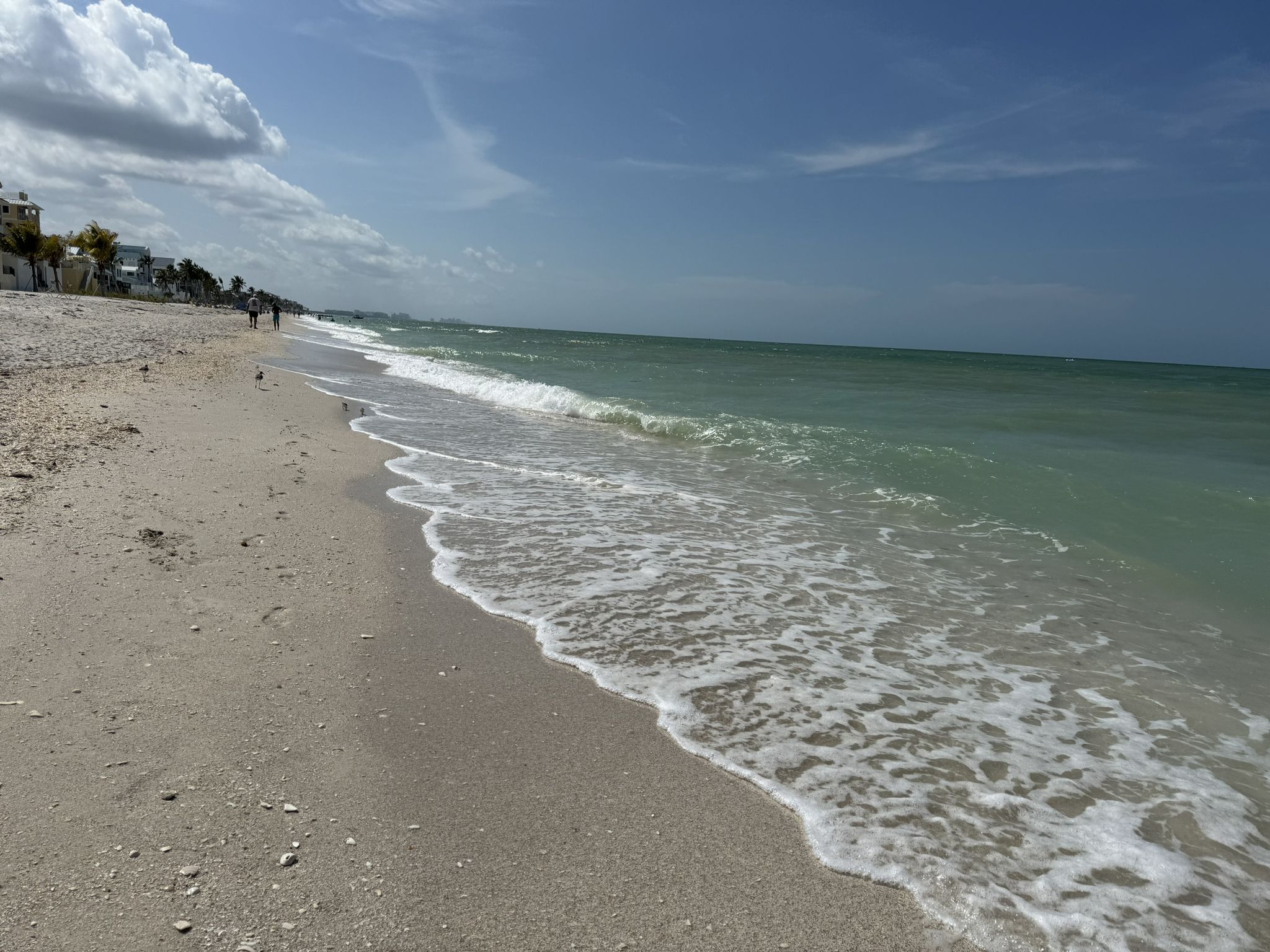 Bright beach scene with turquoise ocean waves and distant buildings under a blue sky. - Bonita Beach Walk