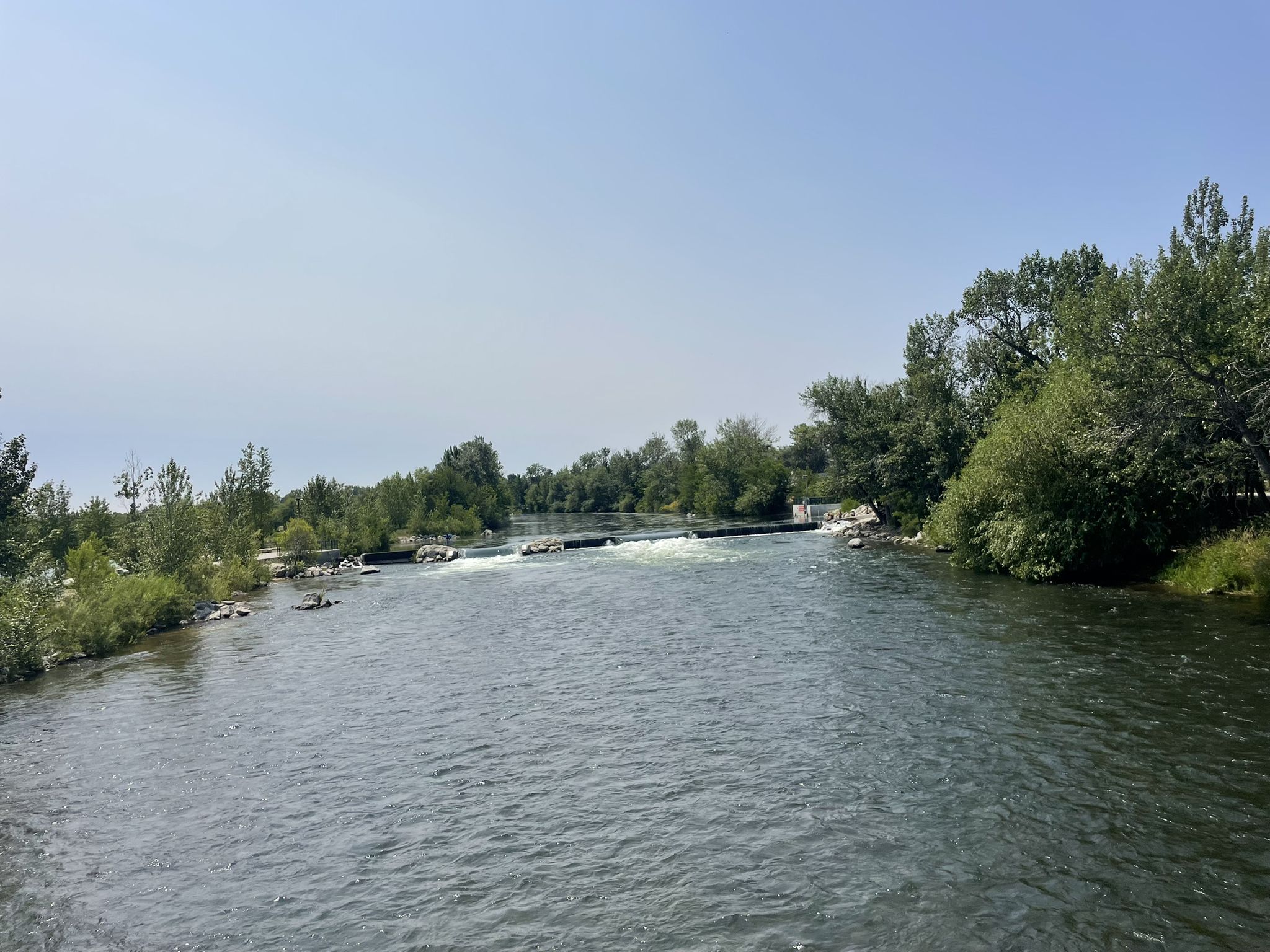 A wide river flows under a clear sky, bordered by green trees. - Boise River Greenbelt – Quinn's Pond loop from Garden City