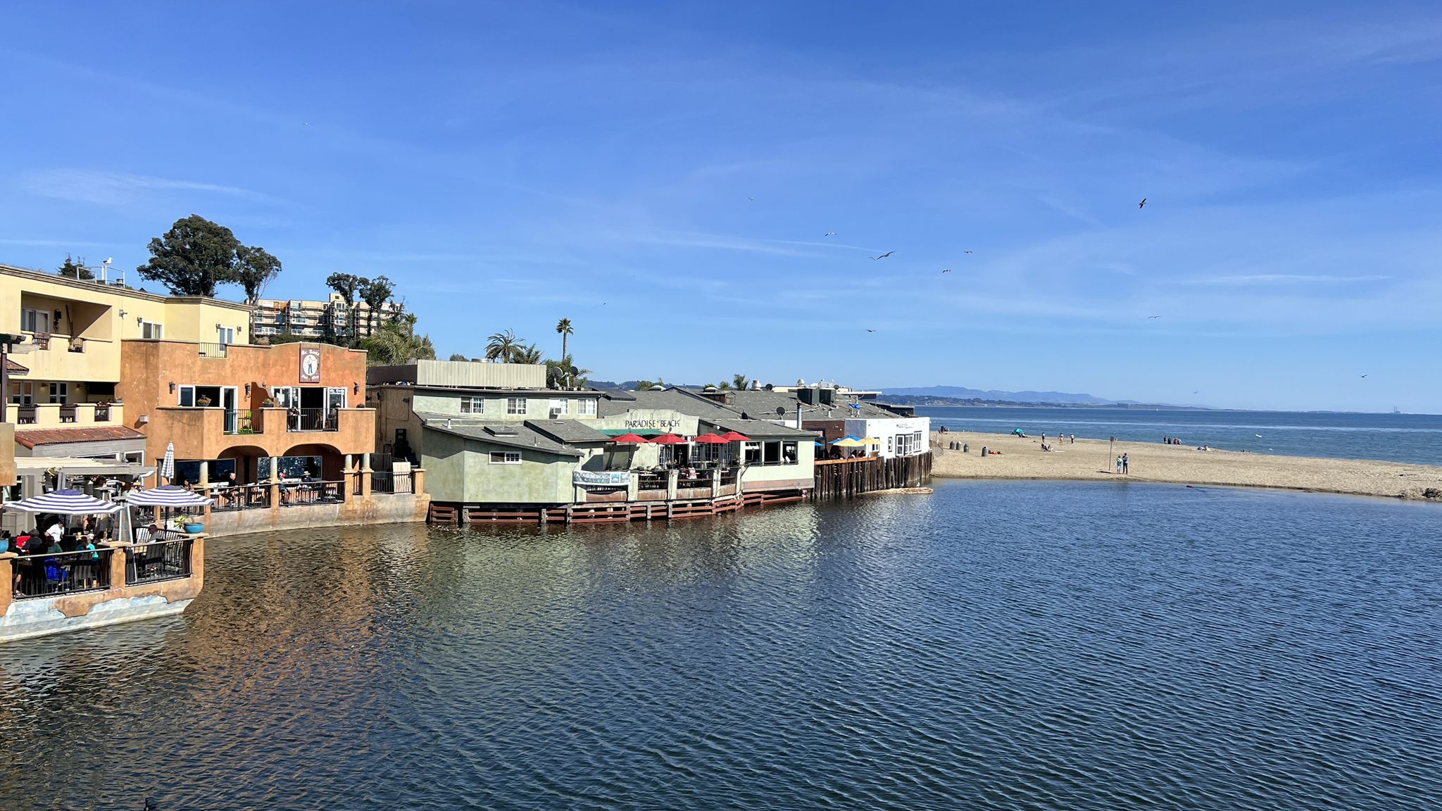 Waterfront buildings next to calm water and a sunny beach with people. - Esplanade Park and Viewing Point – Capitola Village loop from Santa Cruz Mountains