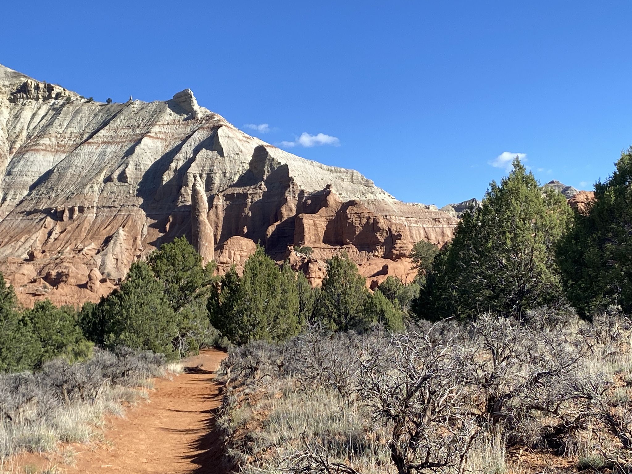 Red dirt path leading to layered rock formations under a clear sky. - Panorama Trail Loop