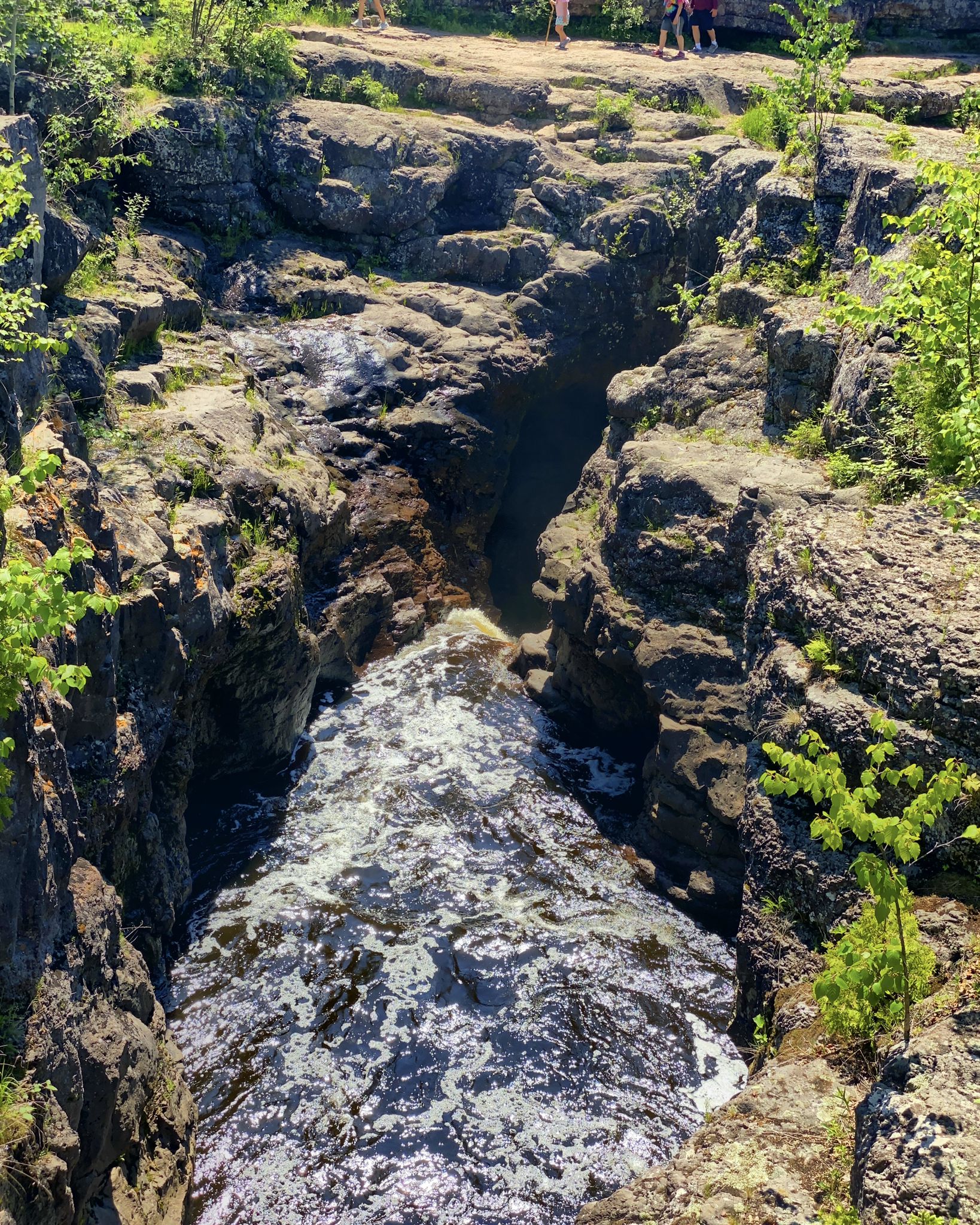 A river rushes through a deep, rocky gorge with people visible on the cliffs. - Temperance River Gorge loop from Poplar River Condos