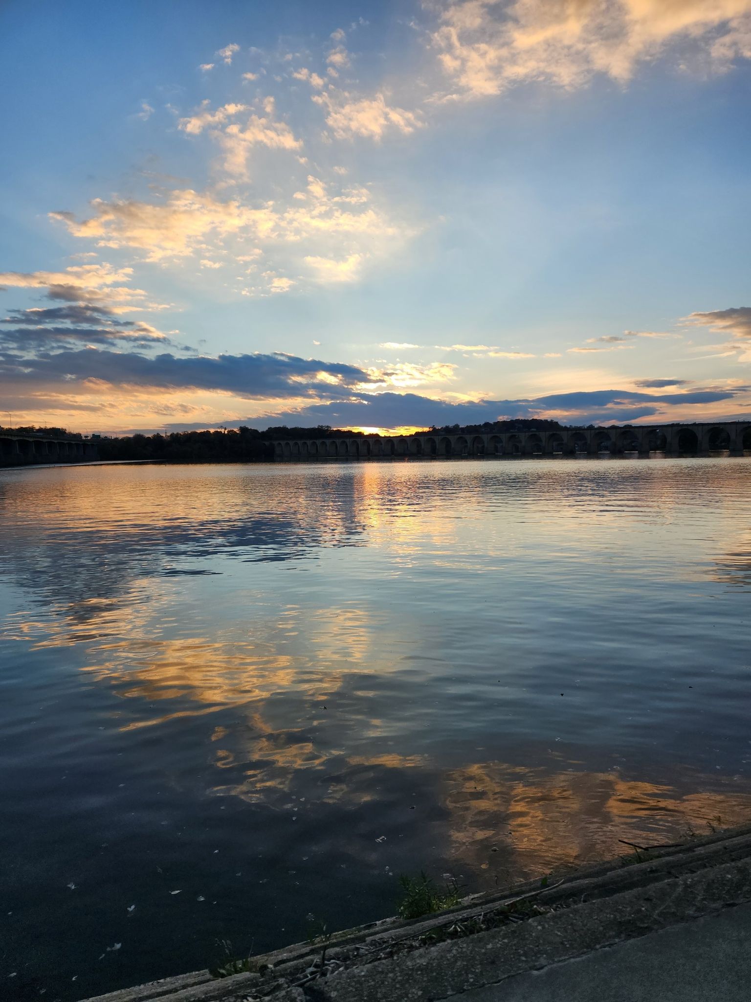 A calm river reflects a vibrant sunset sky with scattered clouds. - Capital Area Greenbelt Loop