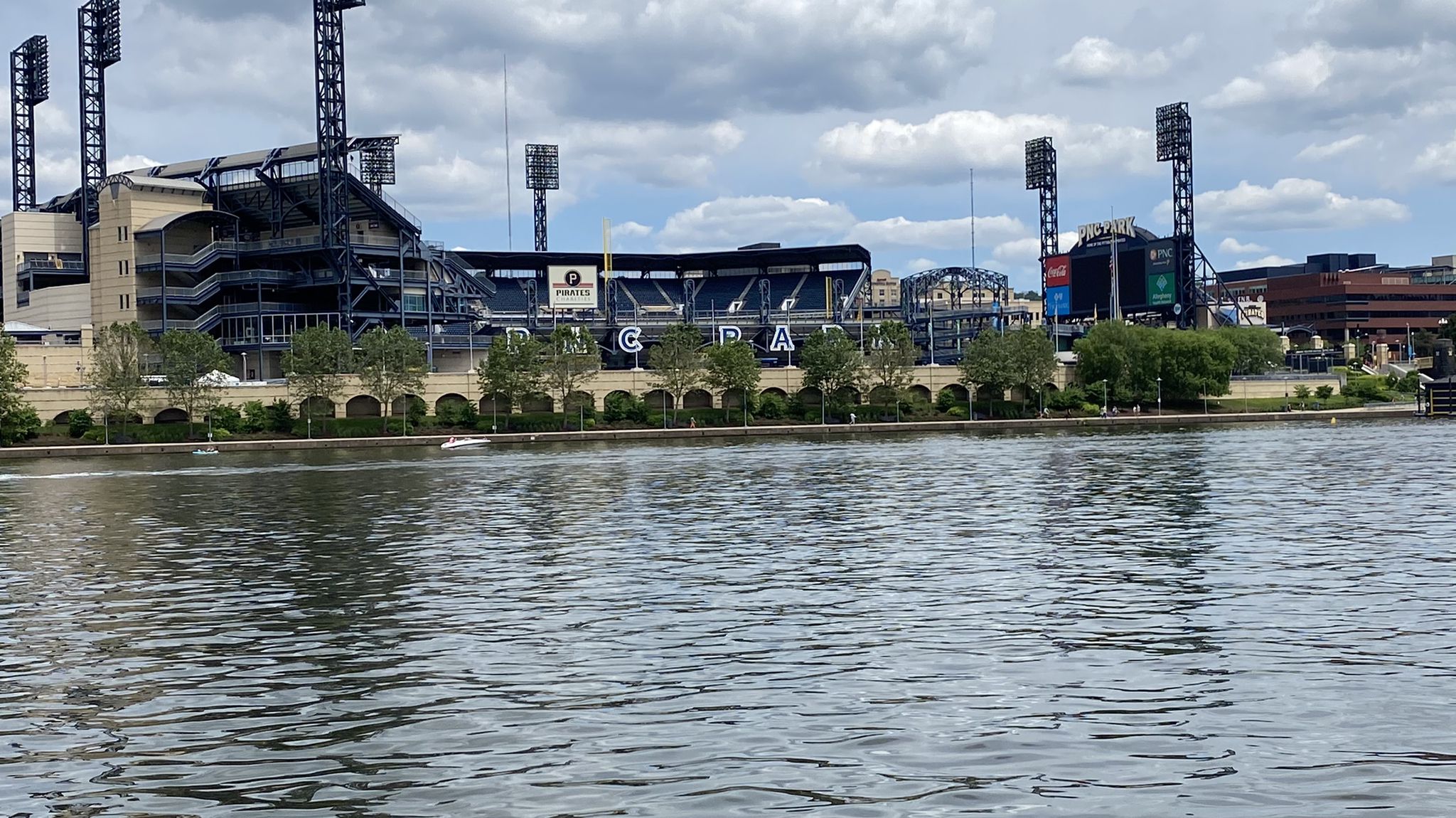 Wide river with a large stadium and city buildings under a cloudy sky. - Riverwalk Point State Park