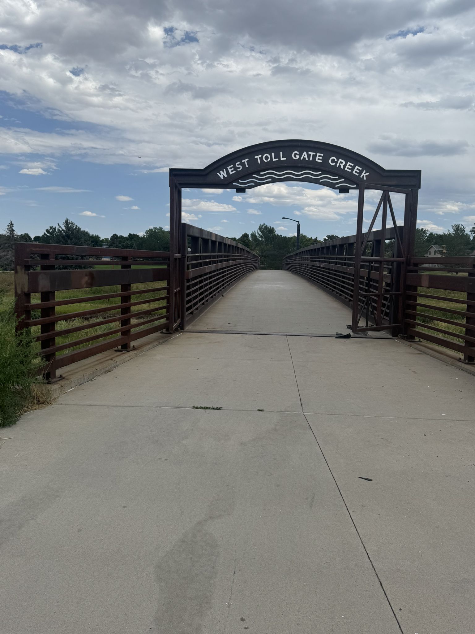 A pedestrian bridge with a sign under a bright, cloudy sky. - Denver Orbital Trail - Segment 15
