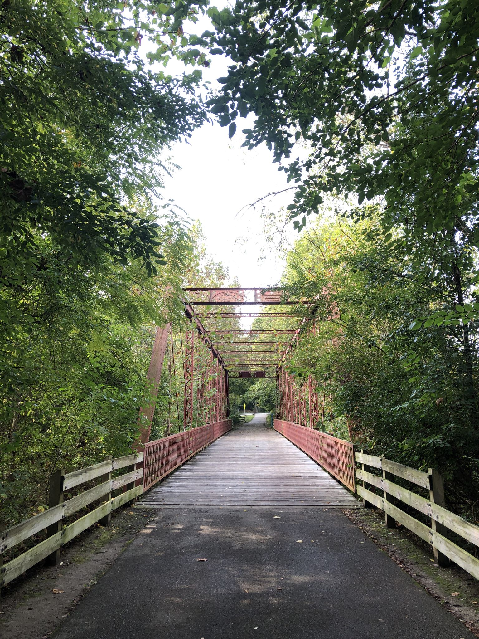 A red metal and wooden bridge surrounded by lush green trees. - Limestone Greenway – Limestone Greenway loop from Bloomington High School South