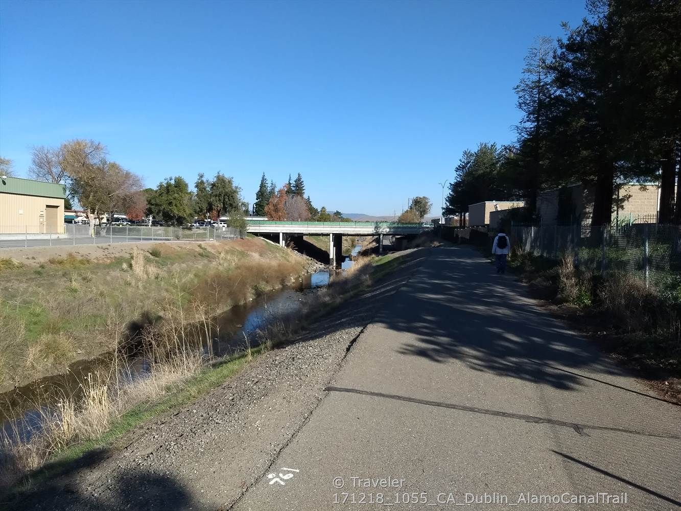 A person walks on a paved path beside a canal and bridge. - Alamo Canal – Arroyo Mocho Trail loop from Dublin/Pleasanton