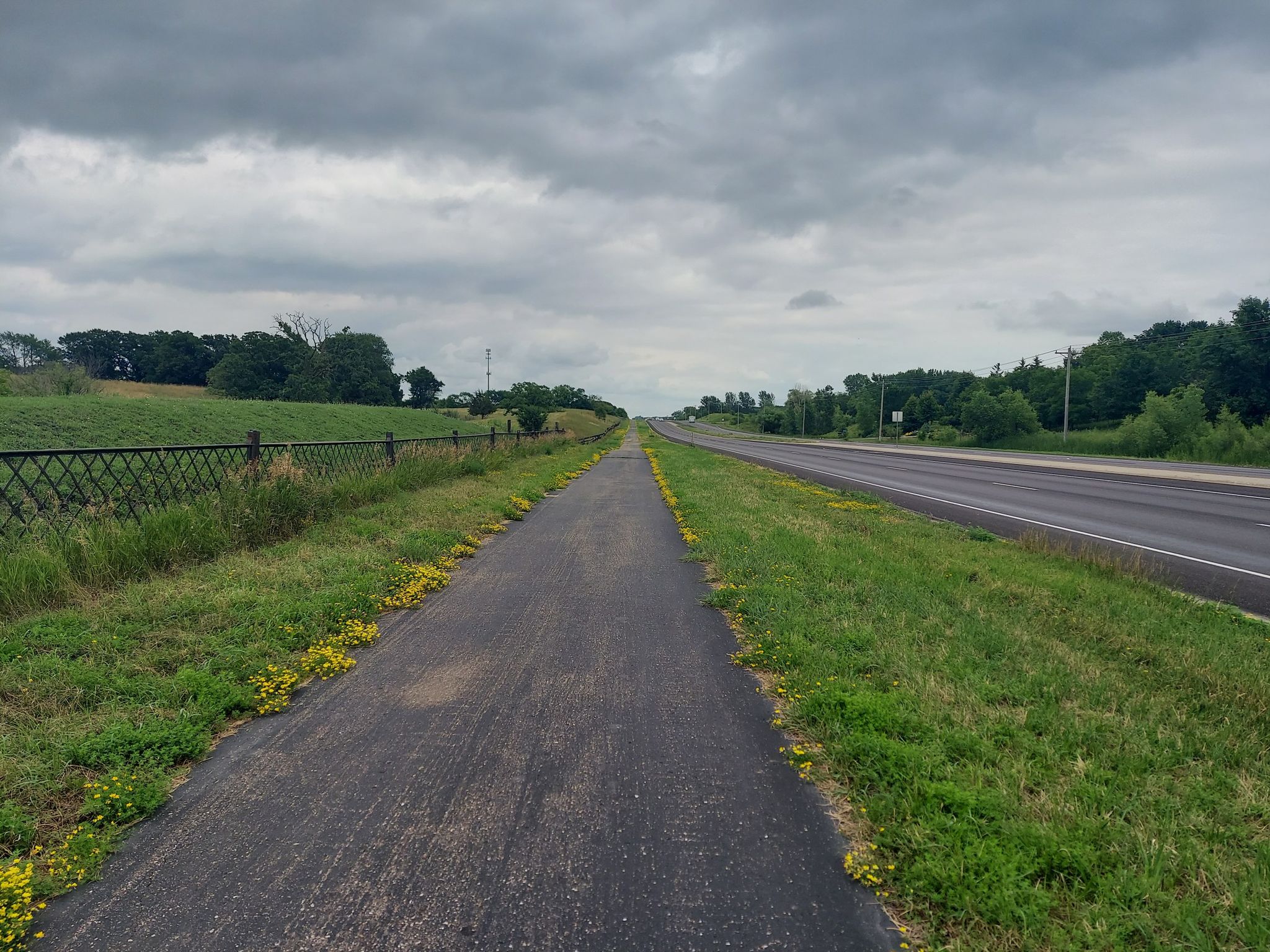 Paved path next to a road and grassy field under a cloudy sky. - Big Woods and Eagle Creek Regional Trails Loop