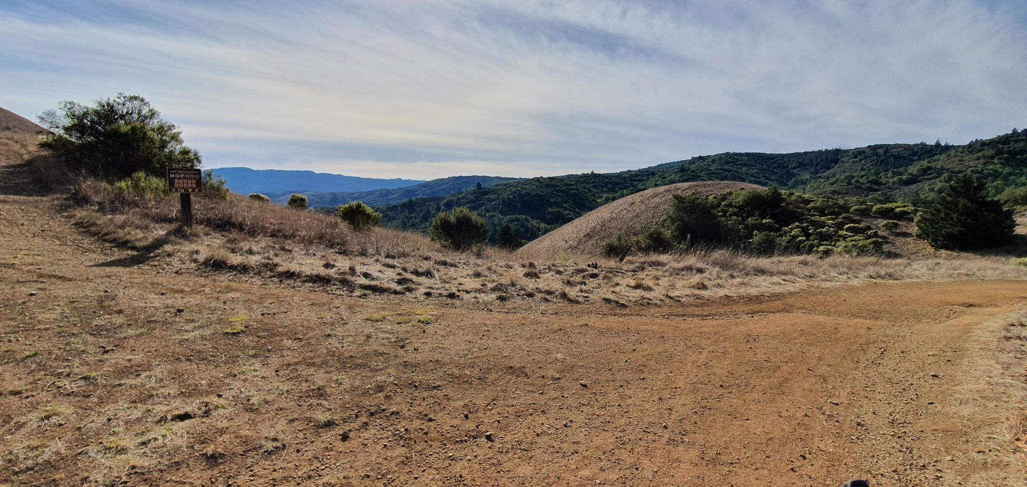A wide dirt path junction on a dry hillside, with distant green mountains under a cloudy sky. - White Hill and Blue Ridge Fire Roads Loop