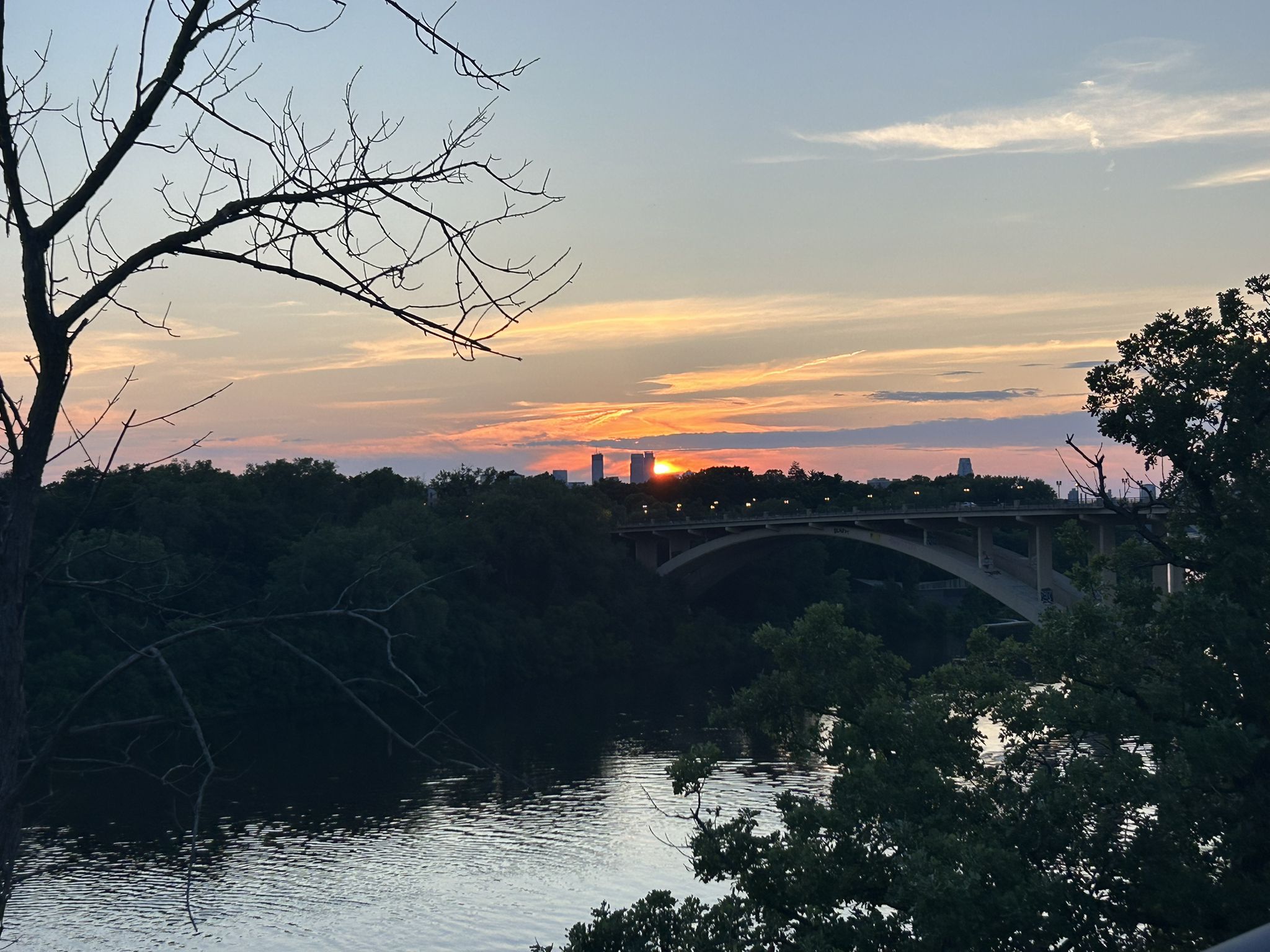 Sunset over a river and a distant bridge, silhouetted trees in foreground. - Shadow Falls Loop