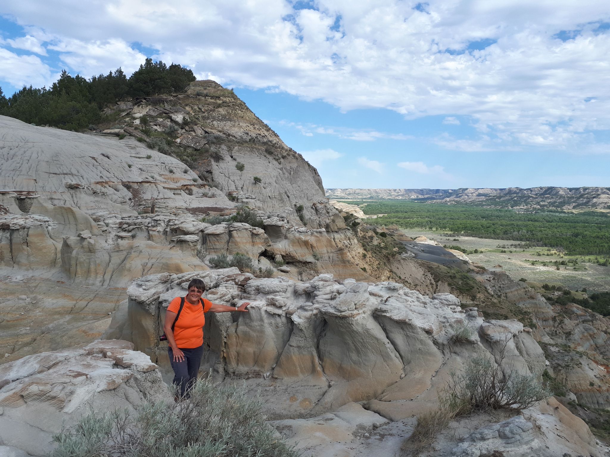 Woman in orange shirt standing on rocky outcrop overlooking a vast valley. - Hiking loop from Riverbend Overlook