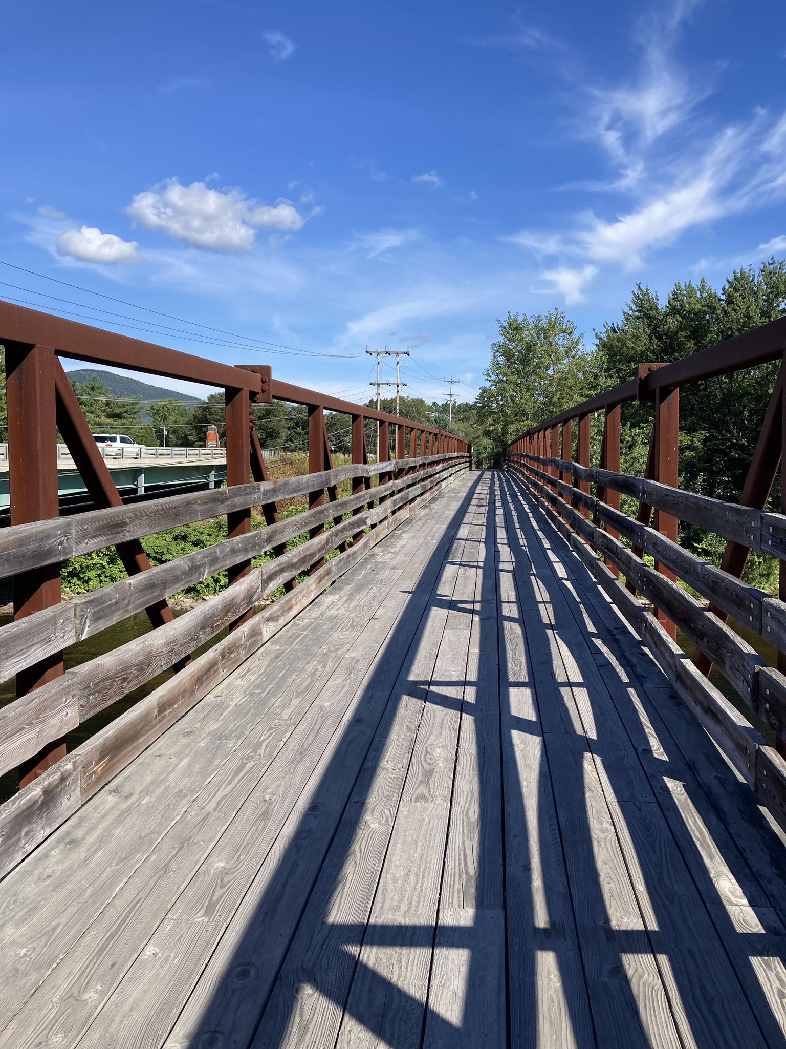 Sunny wooden bridge with long shadows and a bright blue sky. - Bethel Pathway