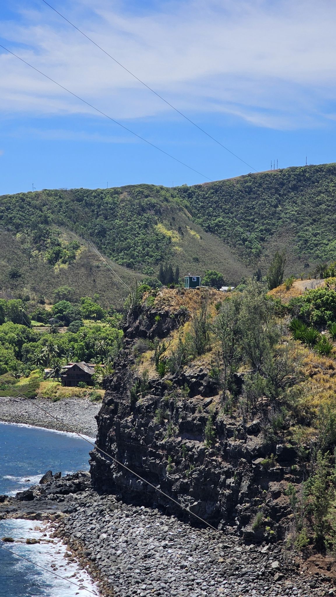 Steep rocky cliff overlooking a pebbled beach and ocean, green hills above. - West Maui loop via  Honoapiʻilani Highway