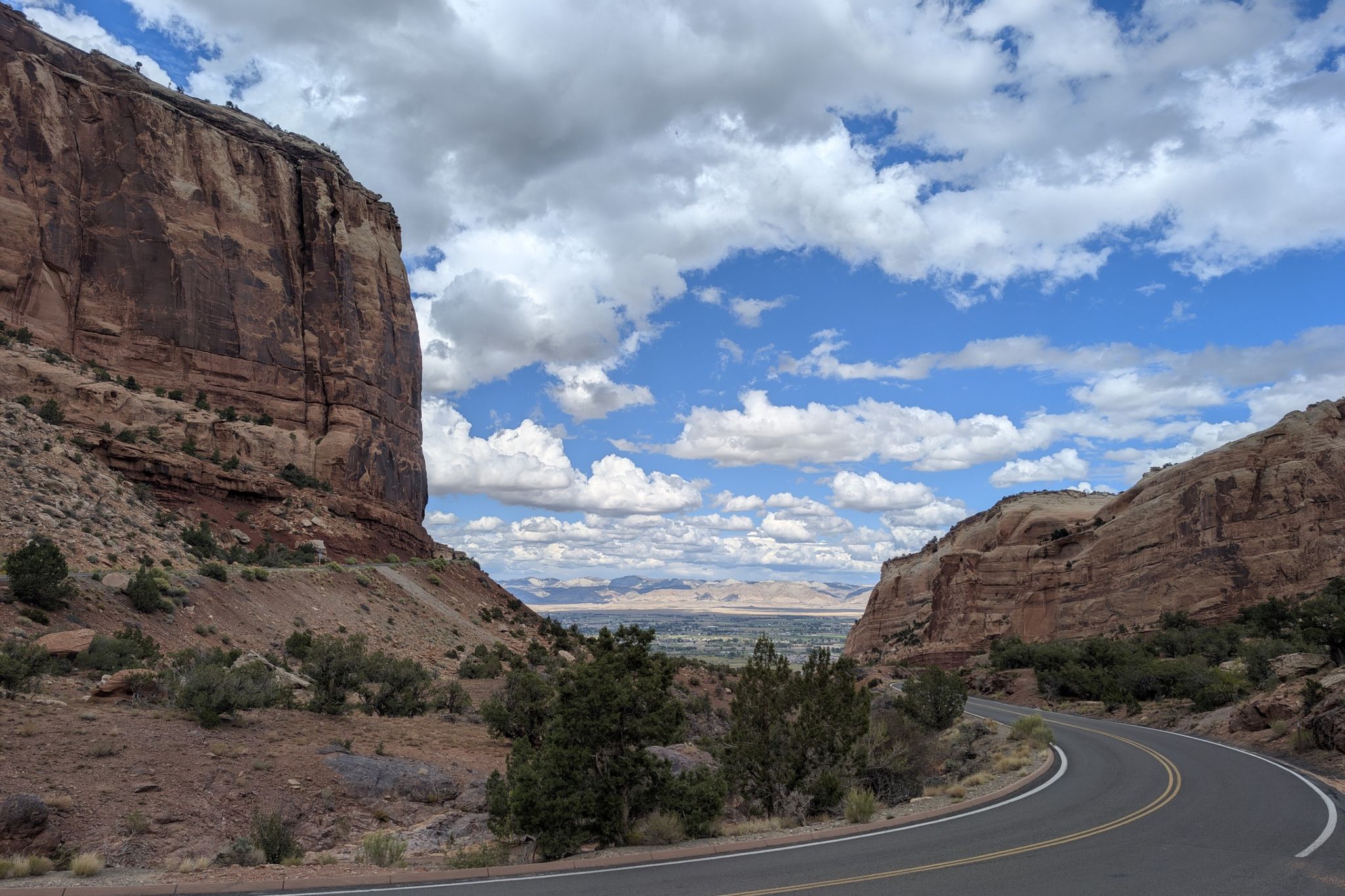 A winding road descends into a green valley between towering red rock cliffs. - Colorado National Monument Visitor Center via Rim Rock Drive