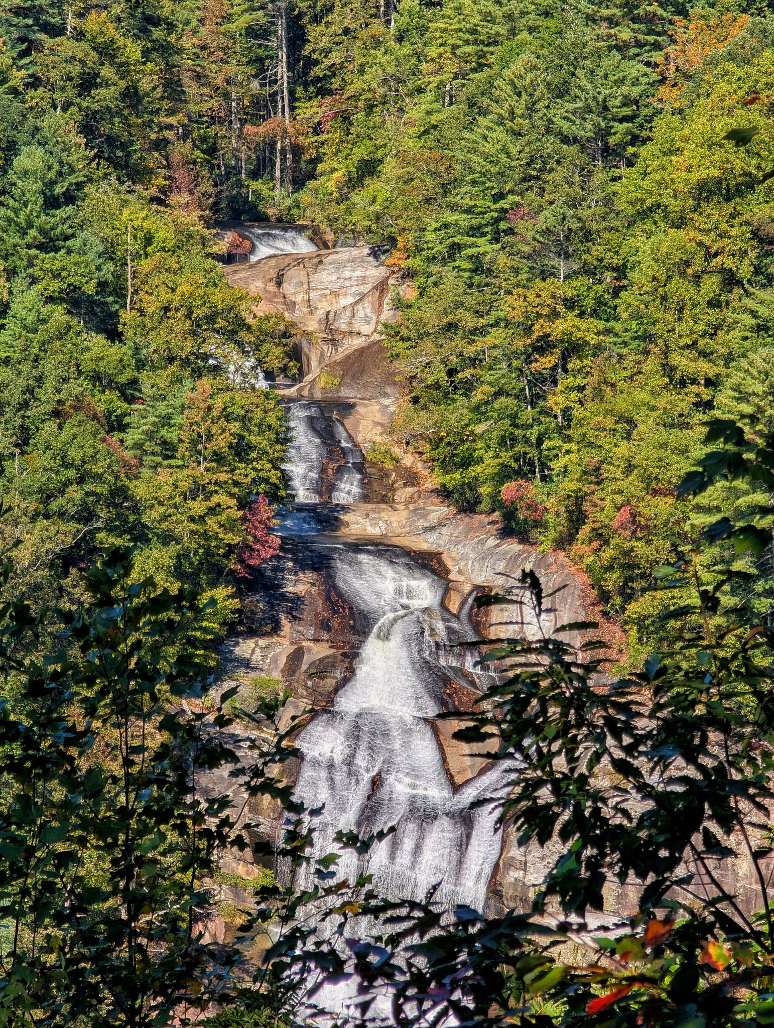 Waterfall cascades down a rocky face surrounded by vibrant green and autumn trees. - Lower Whitewater Falls Trail