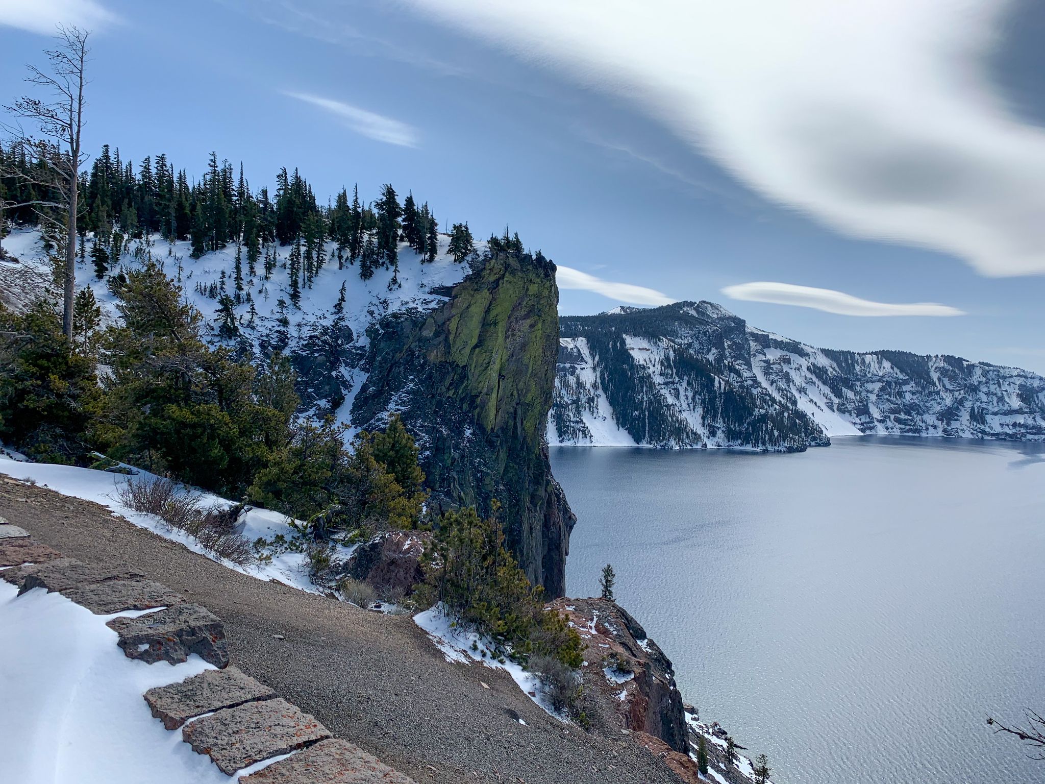 Snowy cliff overlooking a vast lake, with a person on a distant rock. - Cleetwood Cove to Skell Head