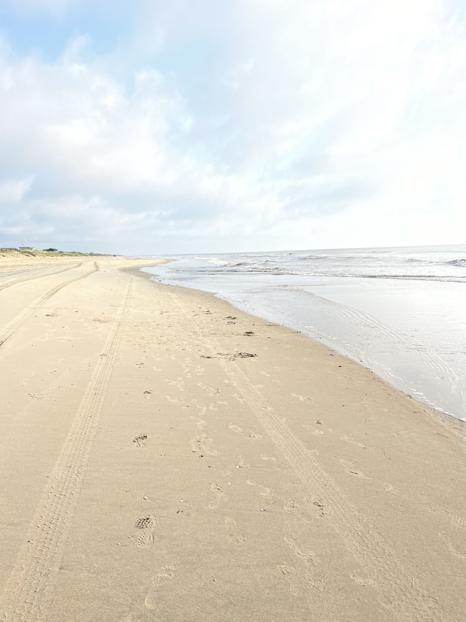 Wide sandy beach with tire tracks next to ocean waves under a cloudy sky. - Corolla North Beach