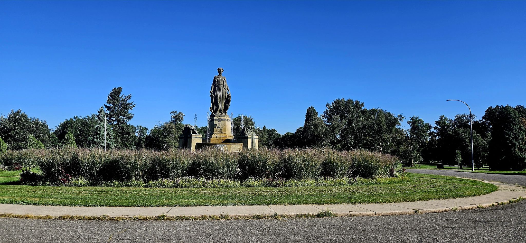 A large statue on a pedestal in a grassy roundabout under a clear blue sky. - Denver City Park Perimeter Loop
