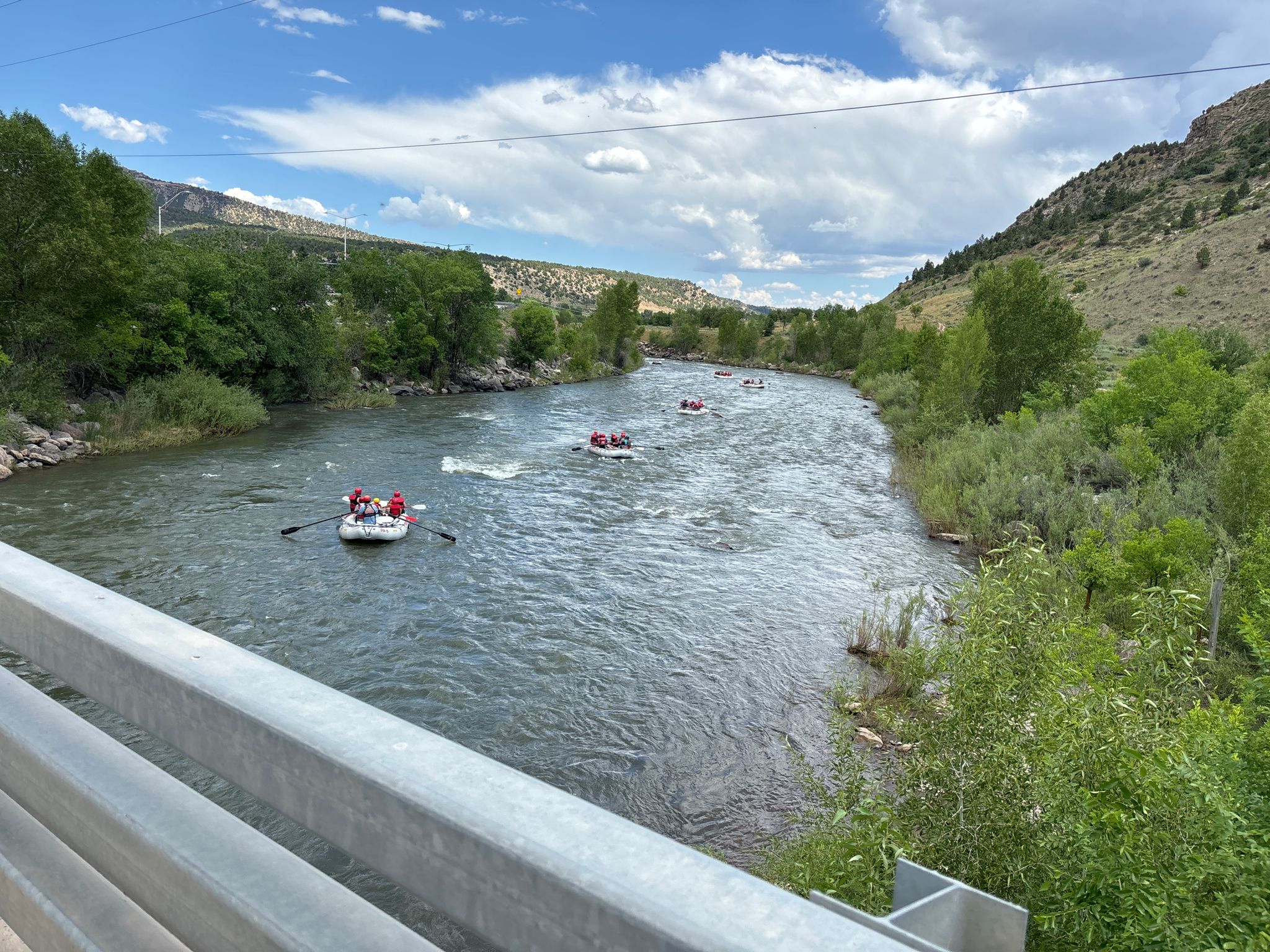 Several rafts with people paddle down a wide river on a bright day. - Smelter Mountain loop