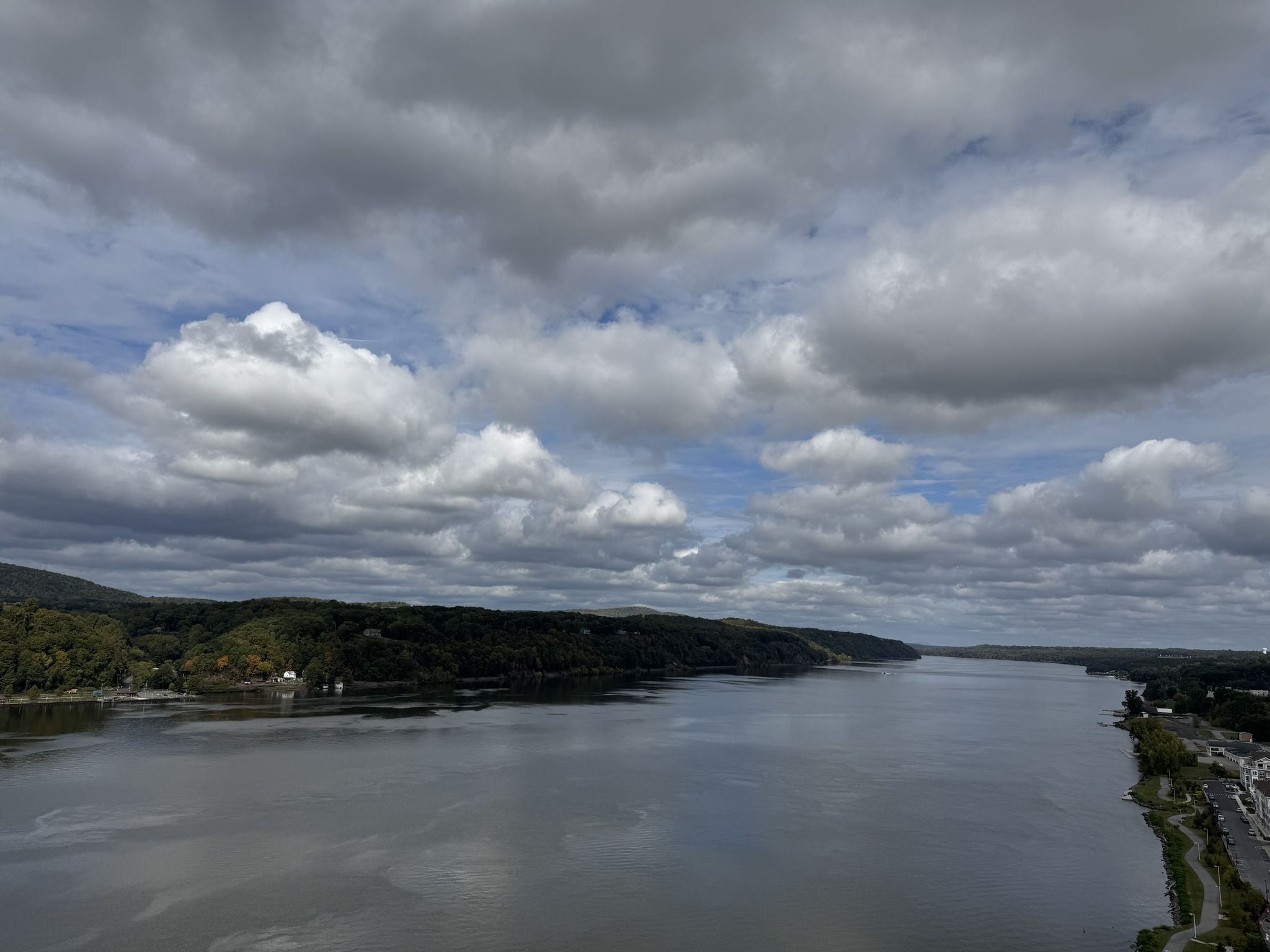 Wide river flowing between forested banks under a dramatic cloudy sky. - Newburgh-Beacon Bridge – Walkway Over the Hudson loop from Beacon