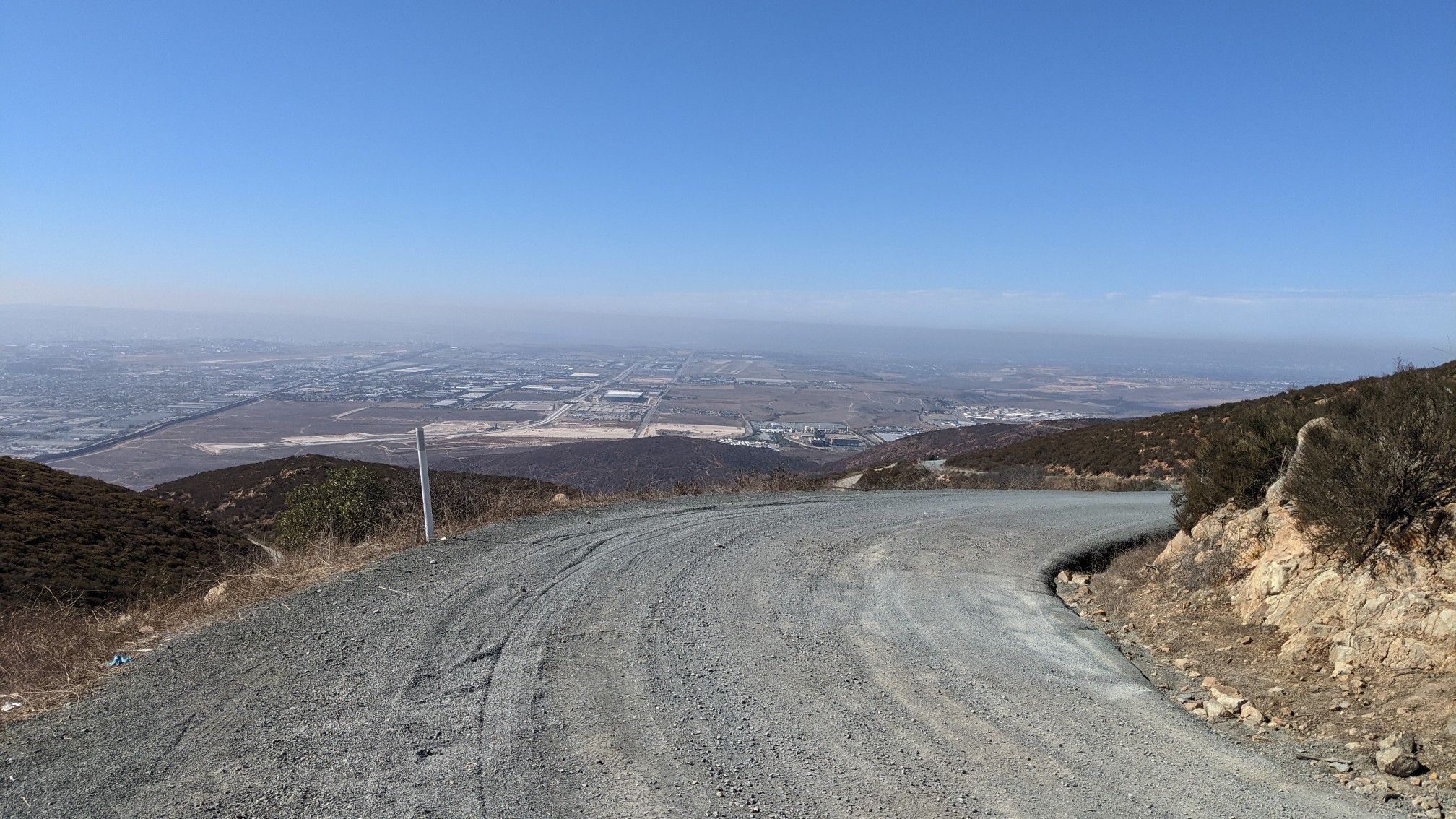 Winding dirt road descends dry hillsides overlooking a distant city on a clear day. - Otay Valley Regional Park – Otay Mountain loop from Palomar Street