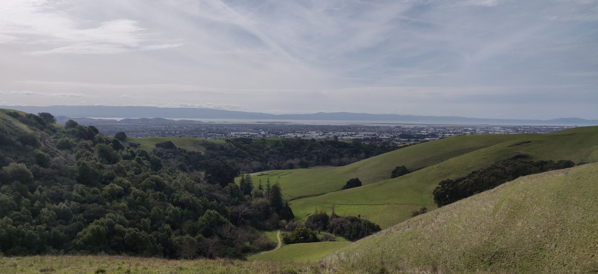 Rolling green hills overlook a distant city and body of water under cloudy skies. - Tolman Peak and South Fork Loop