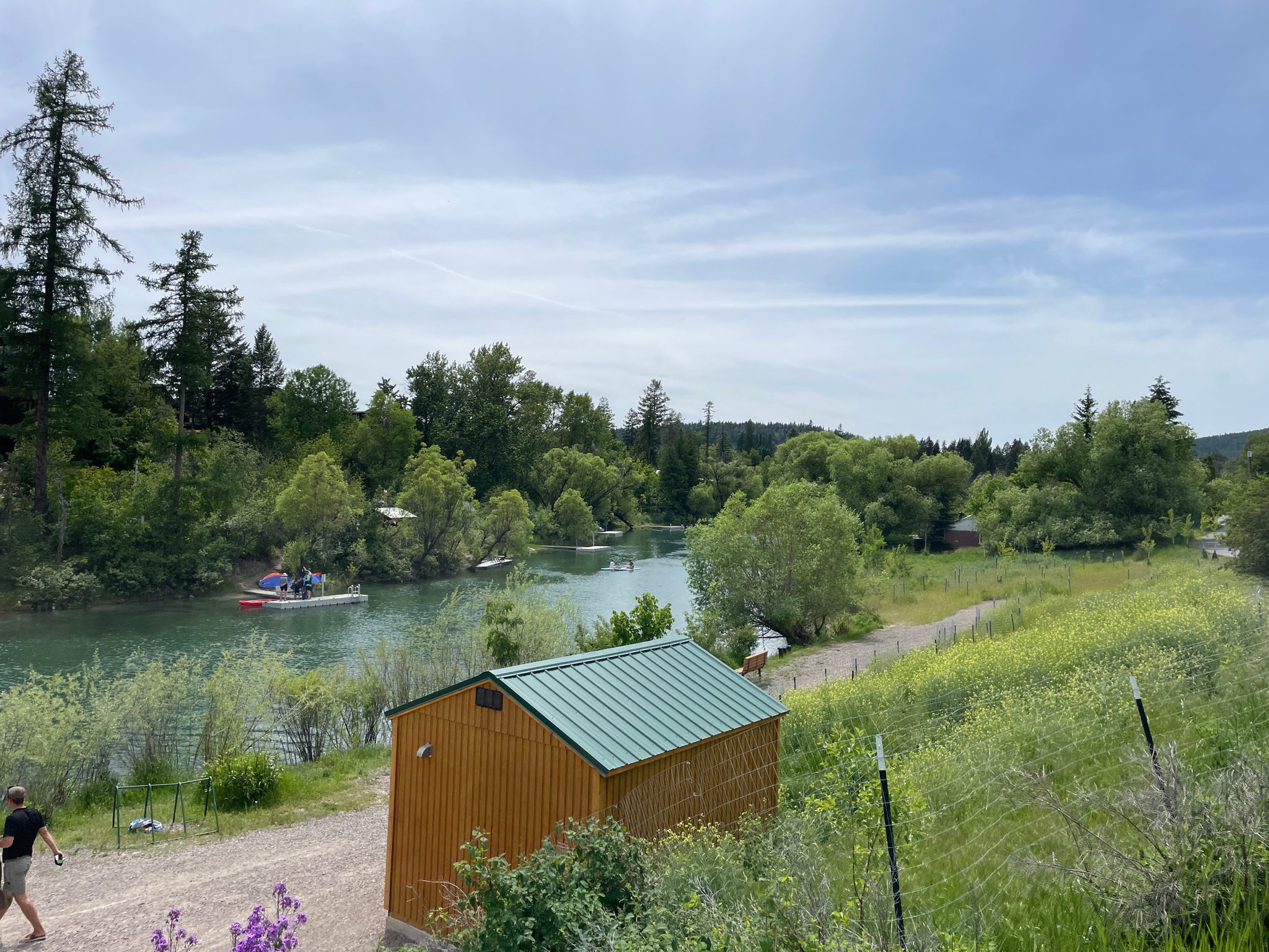 Small wooden shed by a river, with boaters and green landscape. - Great Divide Mountain Bike Route