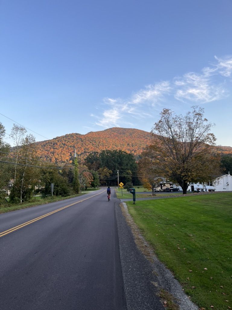 Person cycling on a road towards a mountain with autumn-colored trees. - Beaver Pond loop from Bolton Lower West parking