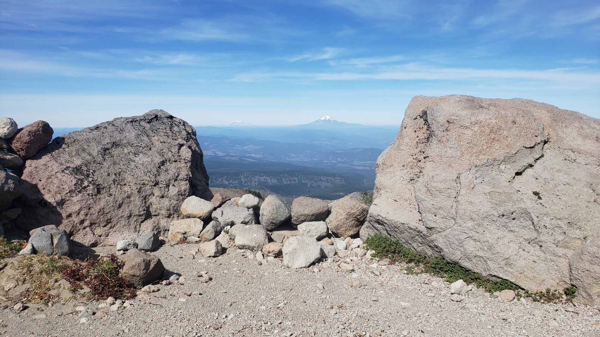 Two large boulders frame a distant mountain range under a bright, clear blue sky. - Cooper Spur Trail