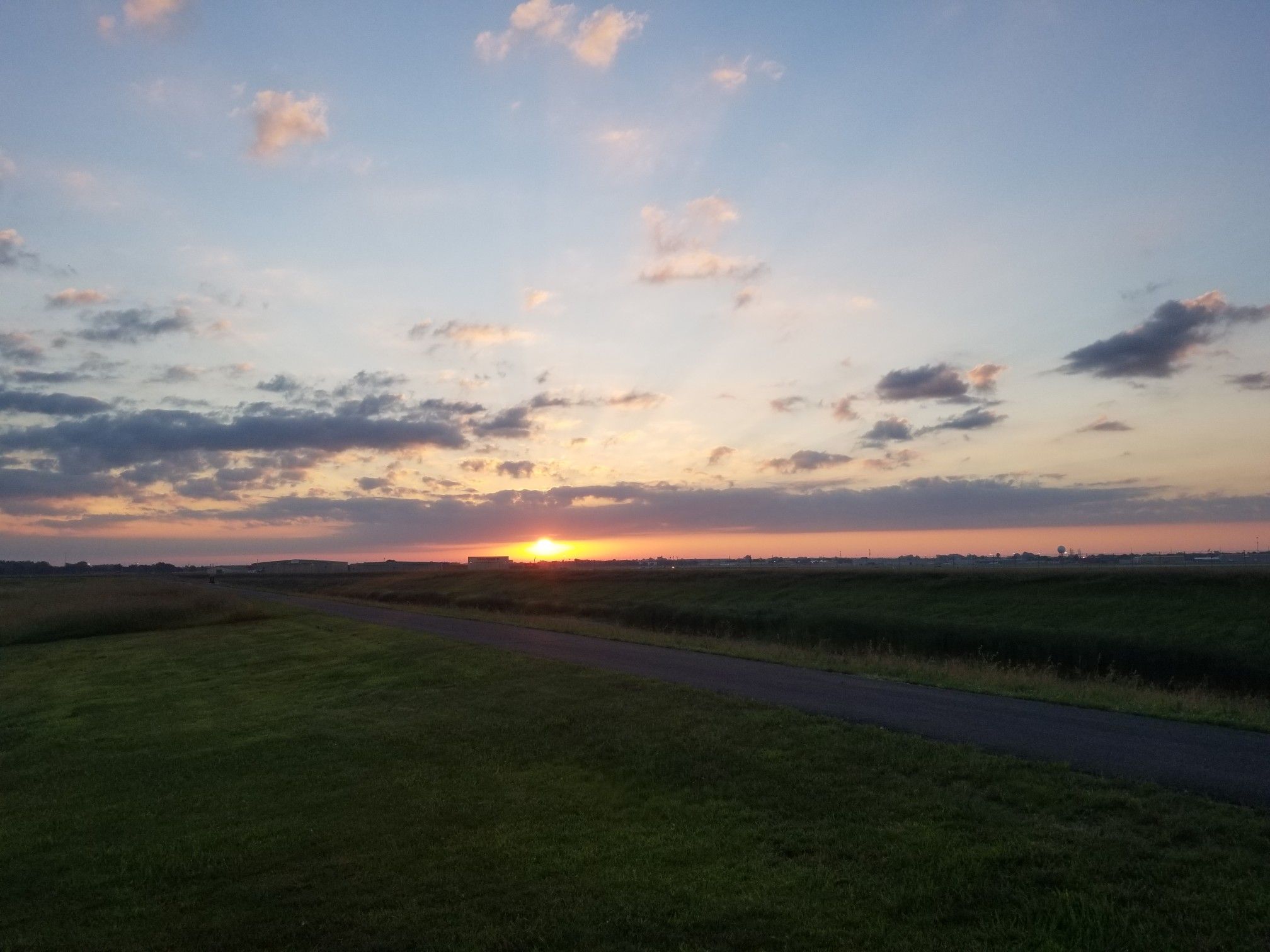 Golden sunset over a flat, grassy landscape with a paved road. - Palisades State Park loop
