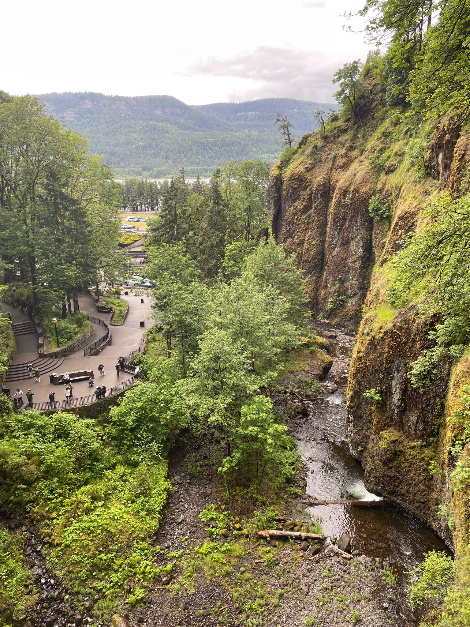 Elevated view of a river, valley, and paved paths with people below. - Multnomah Creek and Waterfall – Multnomah Falls loop from Benson State Recreation Area