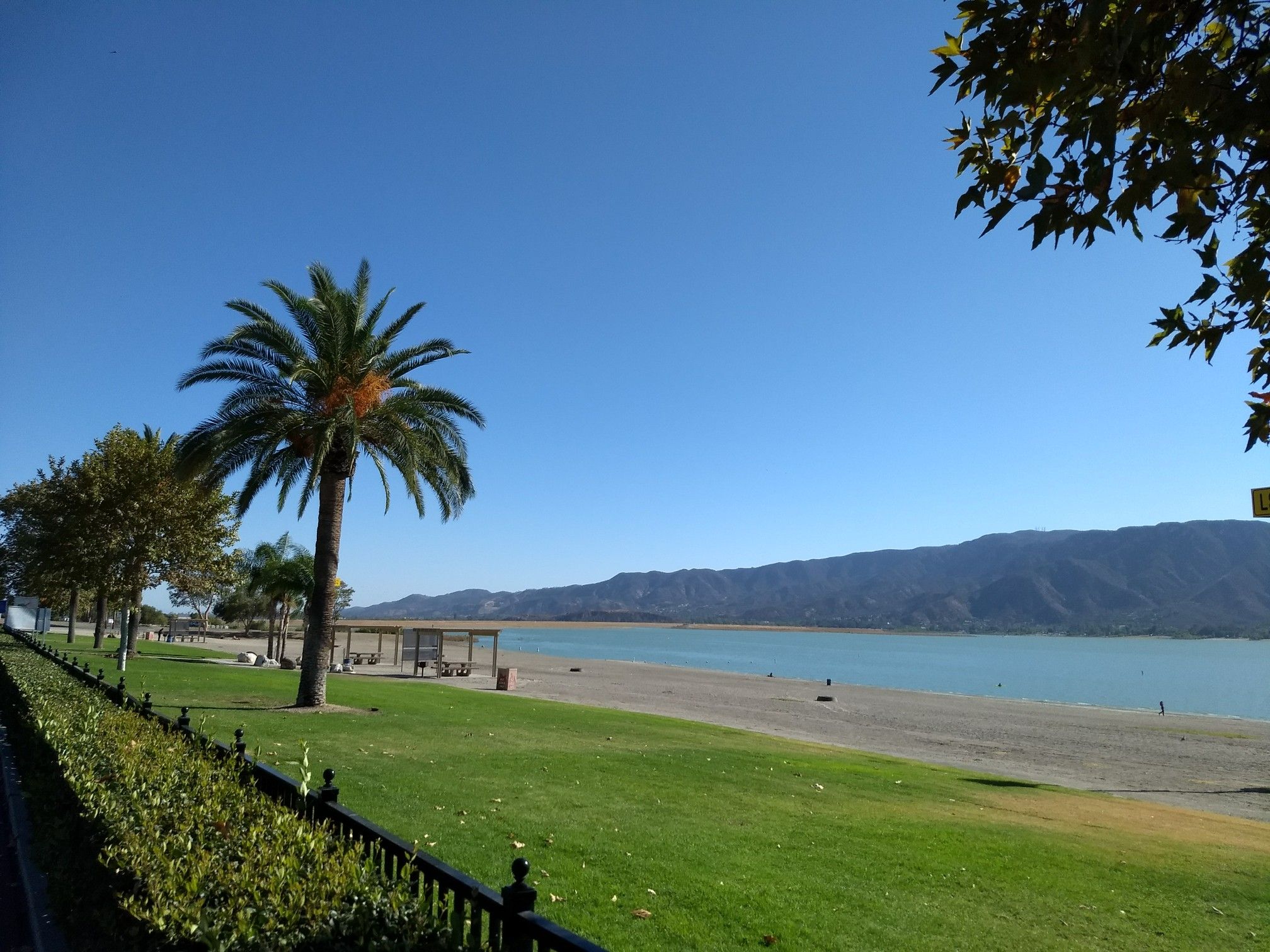 Sunny view of a lake, sandy beach, green lawn, and palm trees. - Historic Downtown Riverwalk (Temescal Wash Trail) loop