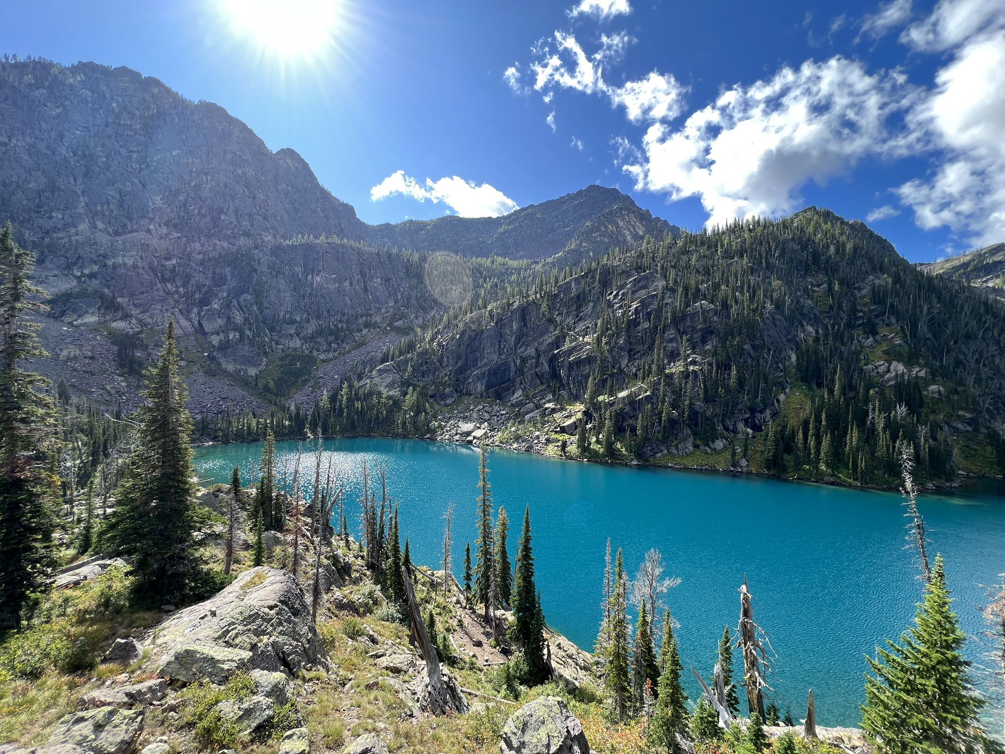 Bright sunny day over a vibrant blue mountain lake surrounded by rocky, forested peaks. - Glacier Lake Trail